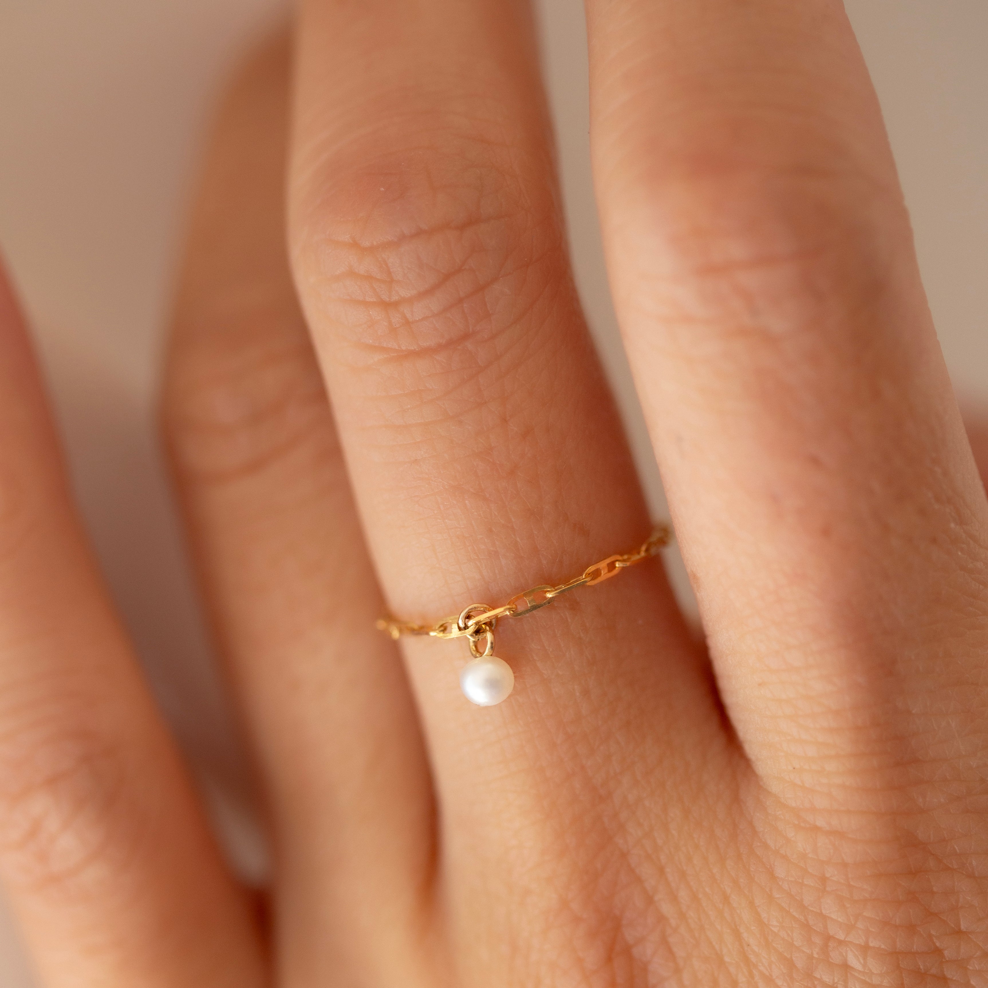 This 14k Solid Gold Chain Ring features a delicate link design and a dainty dangling pearl, creating a modern yet timeless accessory. Worn solo or paired with other rings, it adds a touch of elegance to any look