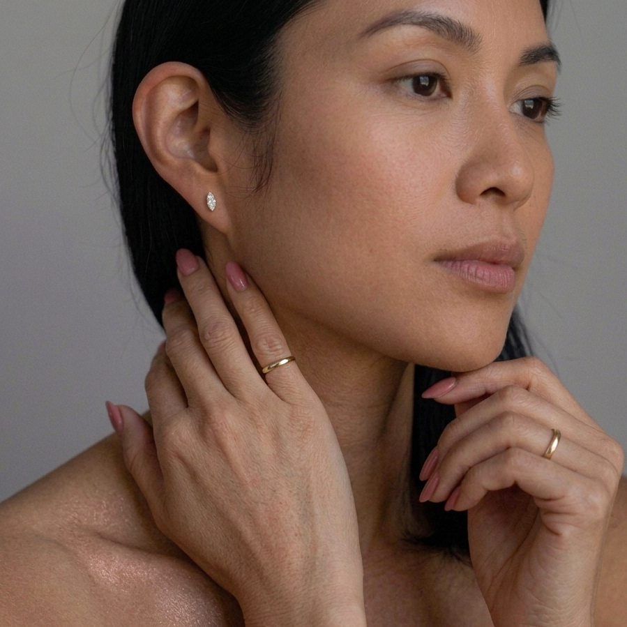 Woman wearing earrings and a ring, with a neutral background