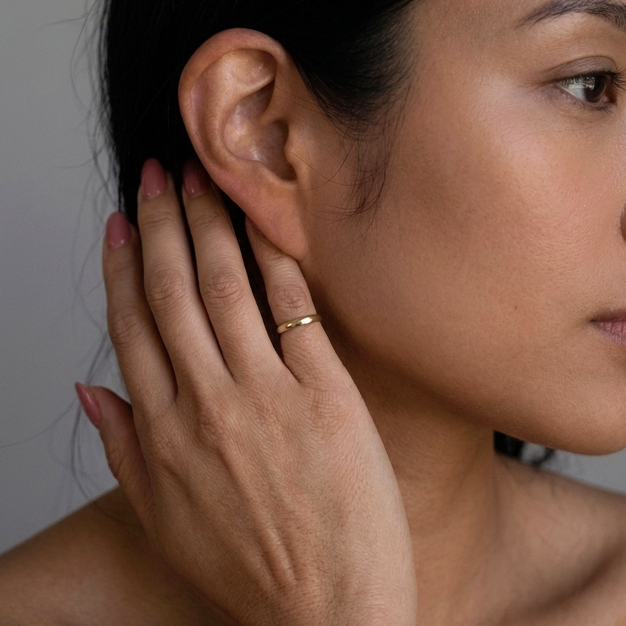 Close-up of a woman's ear with a hand gently touching it, wearing a gold ring.