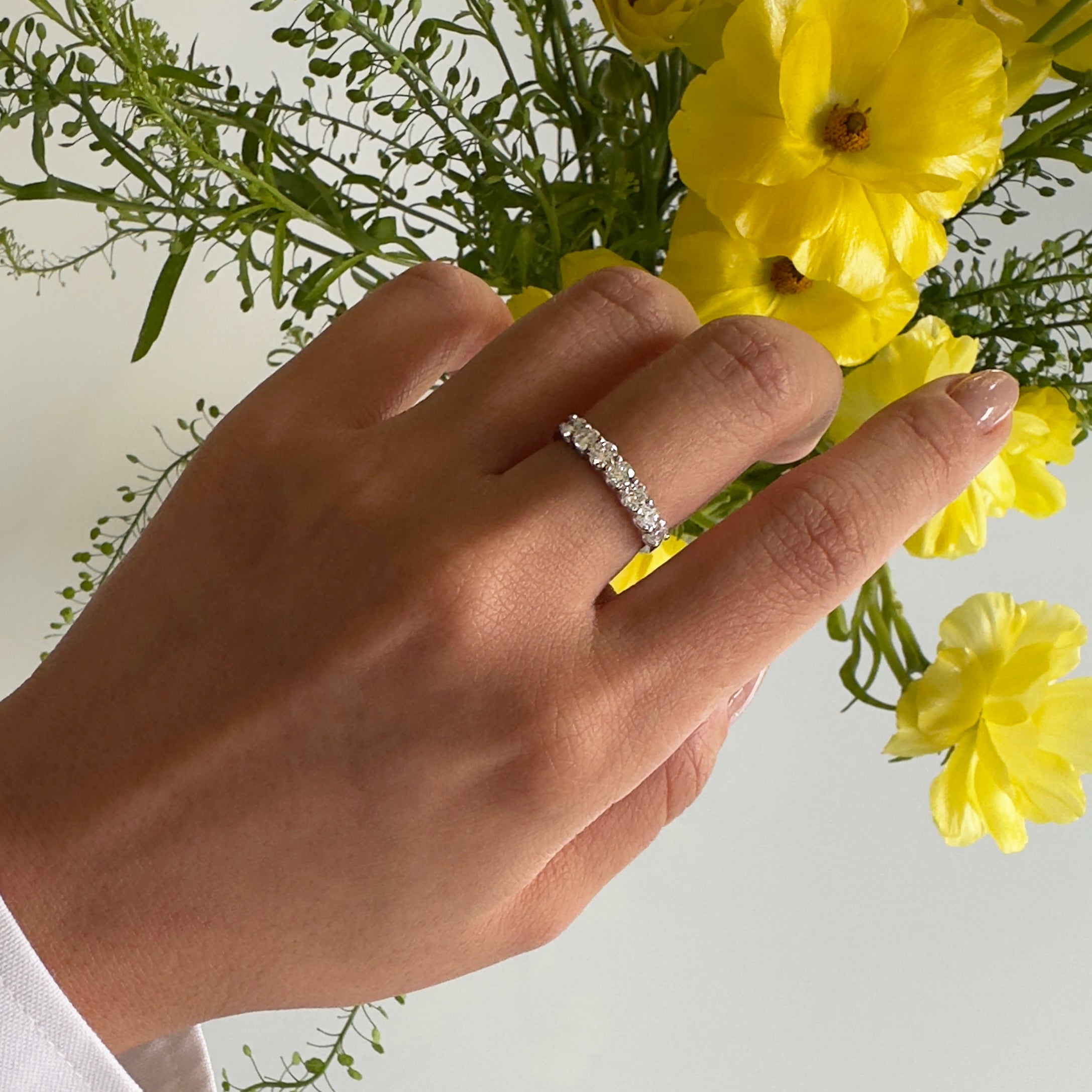 Hand wearing a diamond ring with yellow flowers in the background