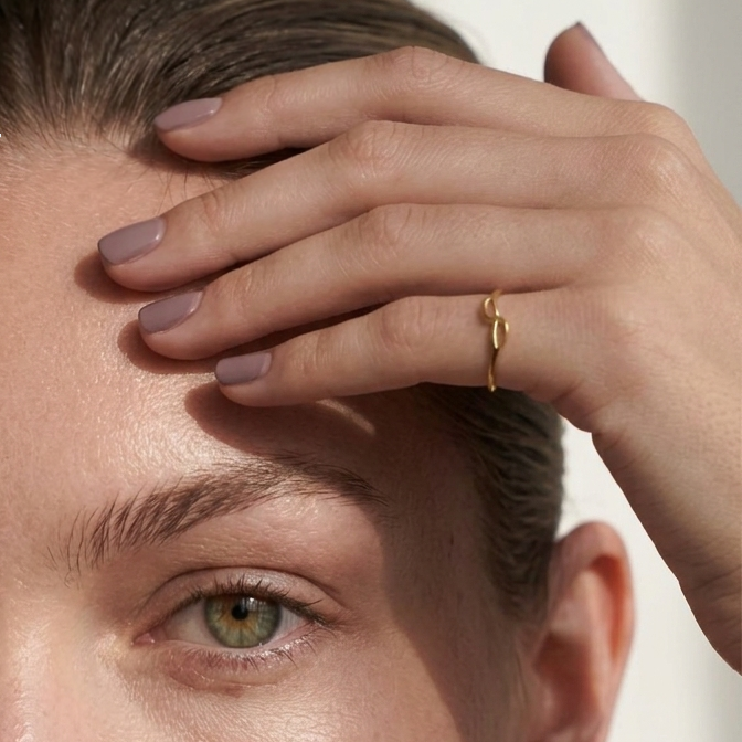 Close-up of a person with a hand on their forehead, wearing a gold ring.