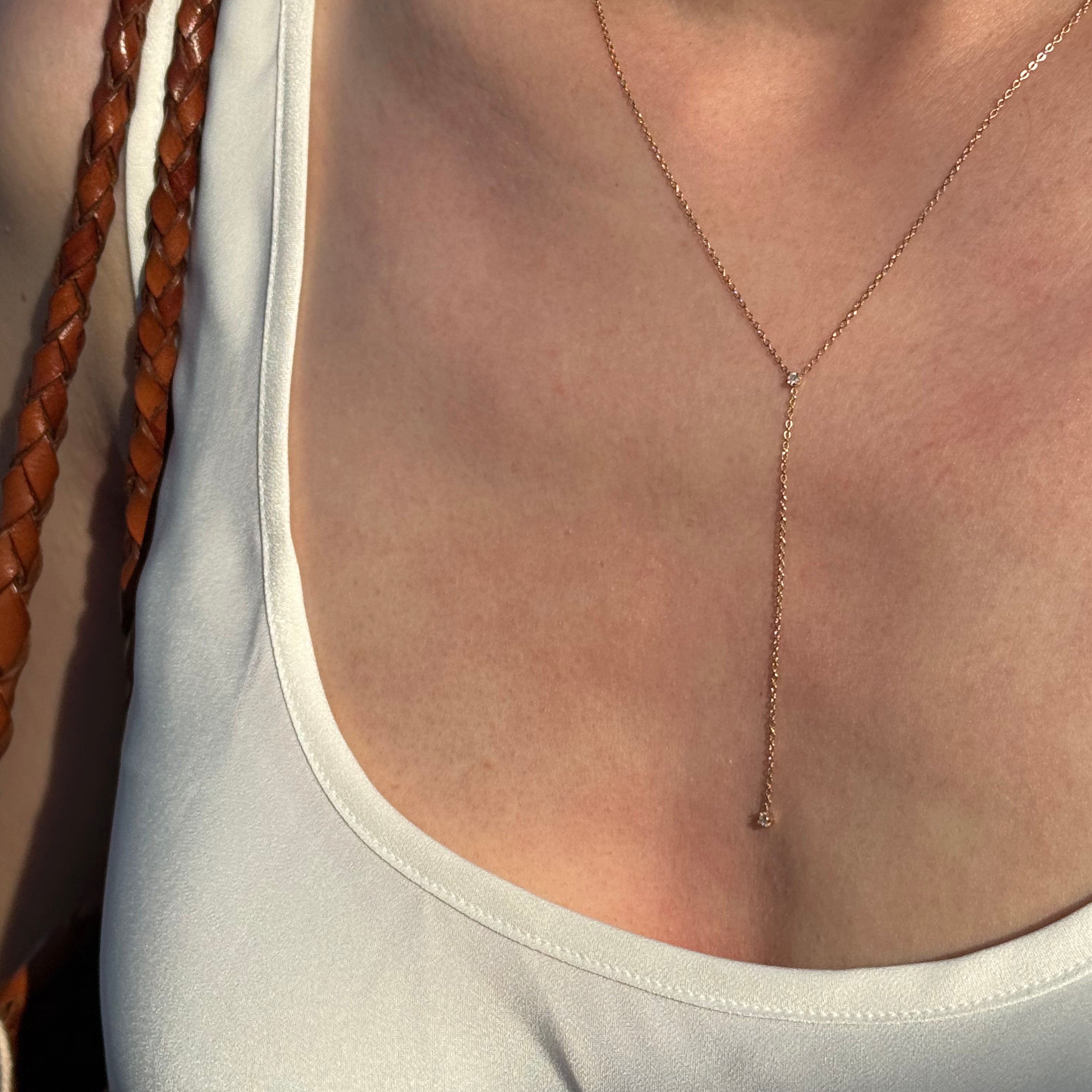 Close-up of a person wearing a thin gold necklace with a neutral background