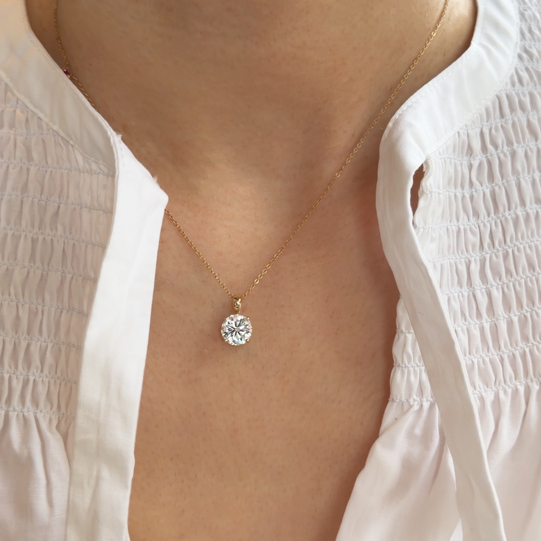 Gold necklace with a diamond pendant worn by a person in a white blouse.