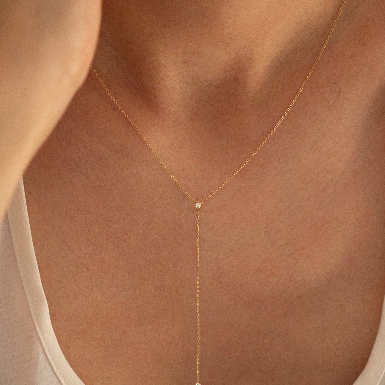 Gold necklace with a small pendant worn by a person in a white top.