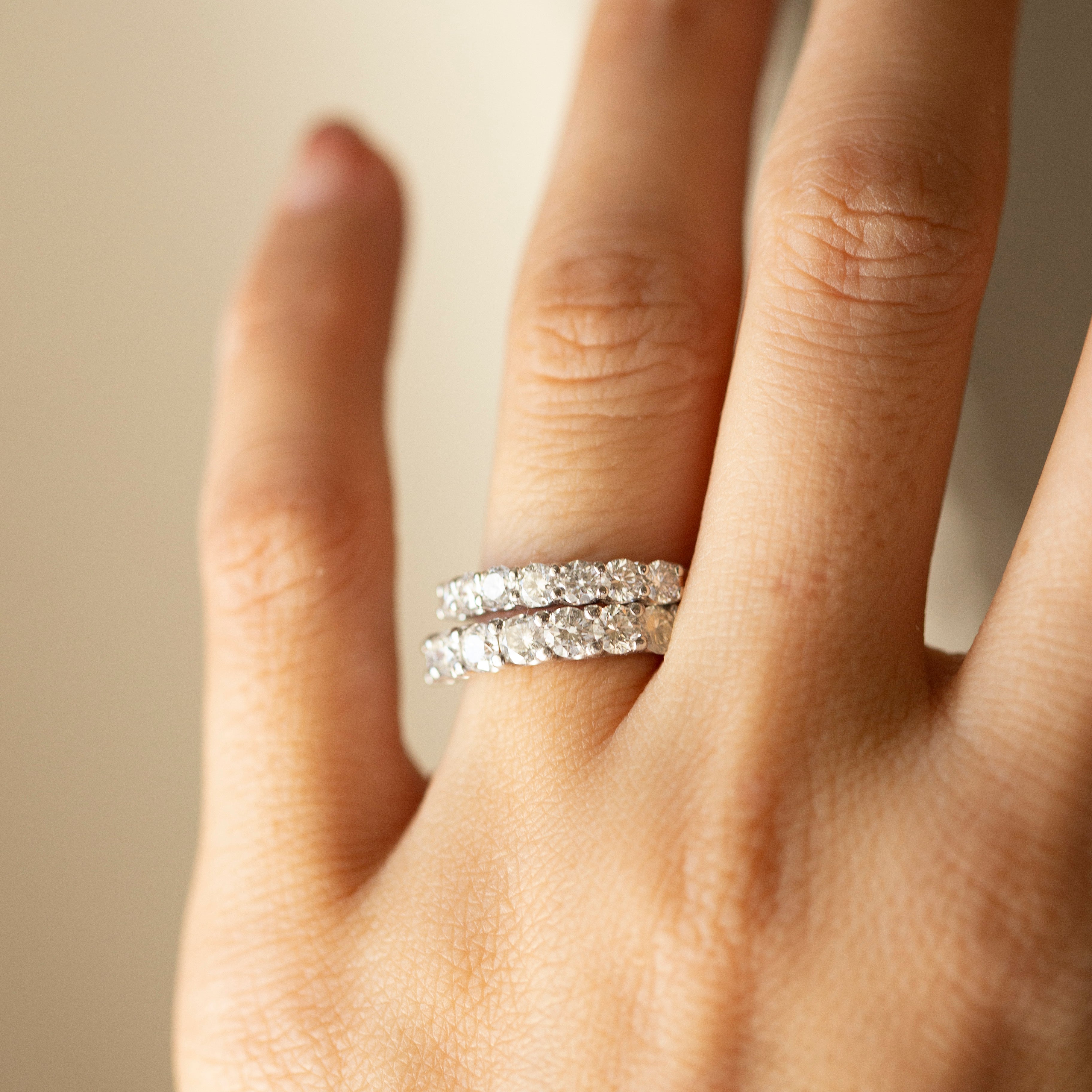 Hand wearing a silver ring with a diamond band on a neutral background