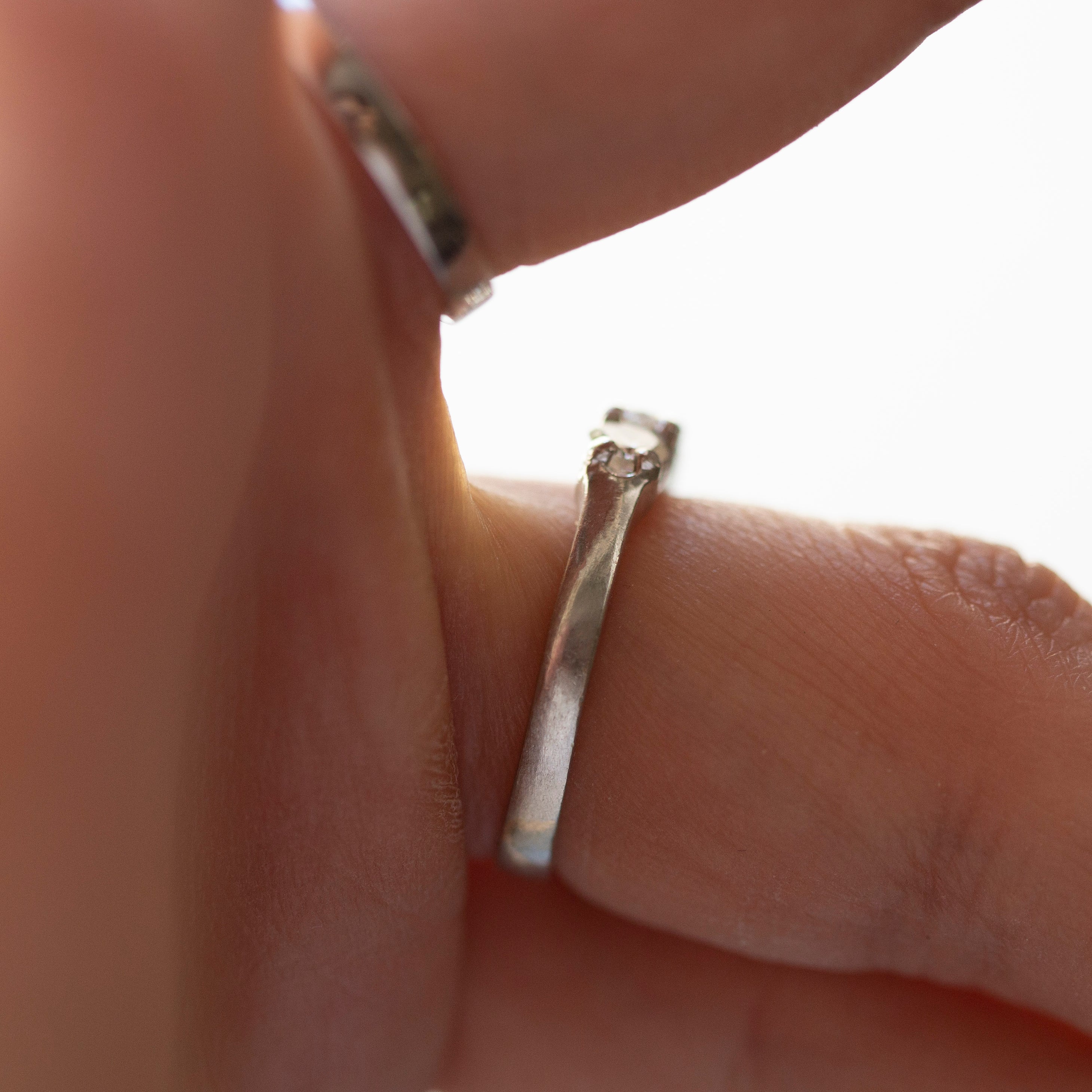Close-up of a hand wearing two silver rings on a light background