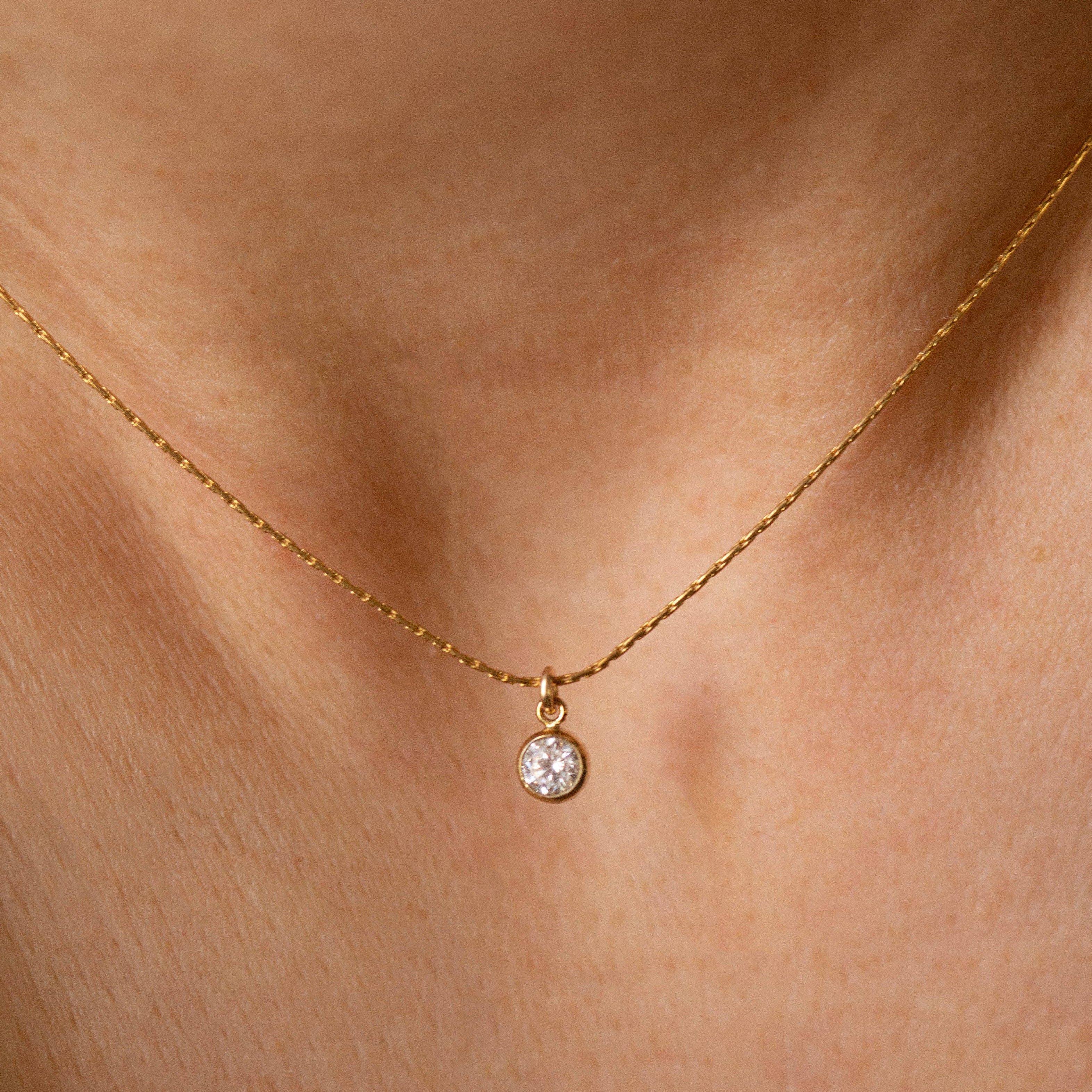 Gold necklace with a small round pendant on a person's neck