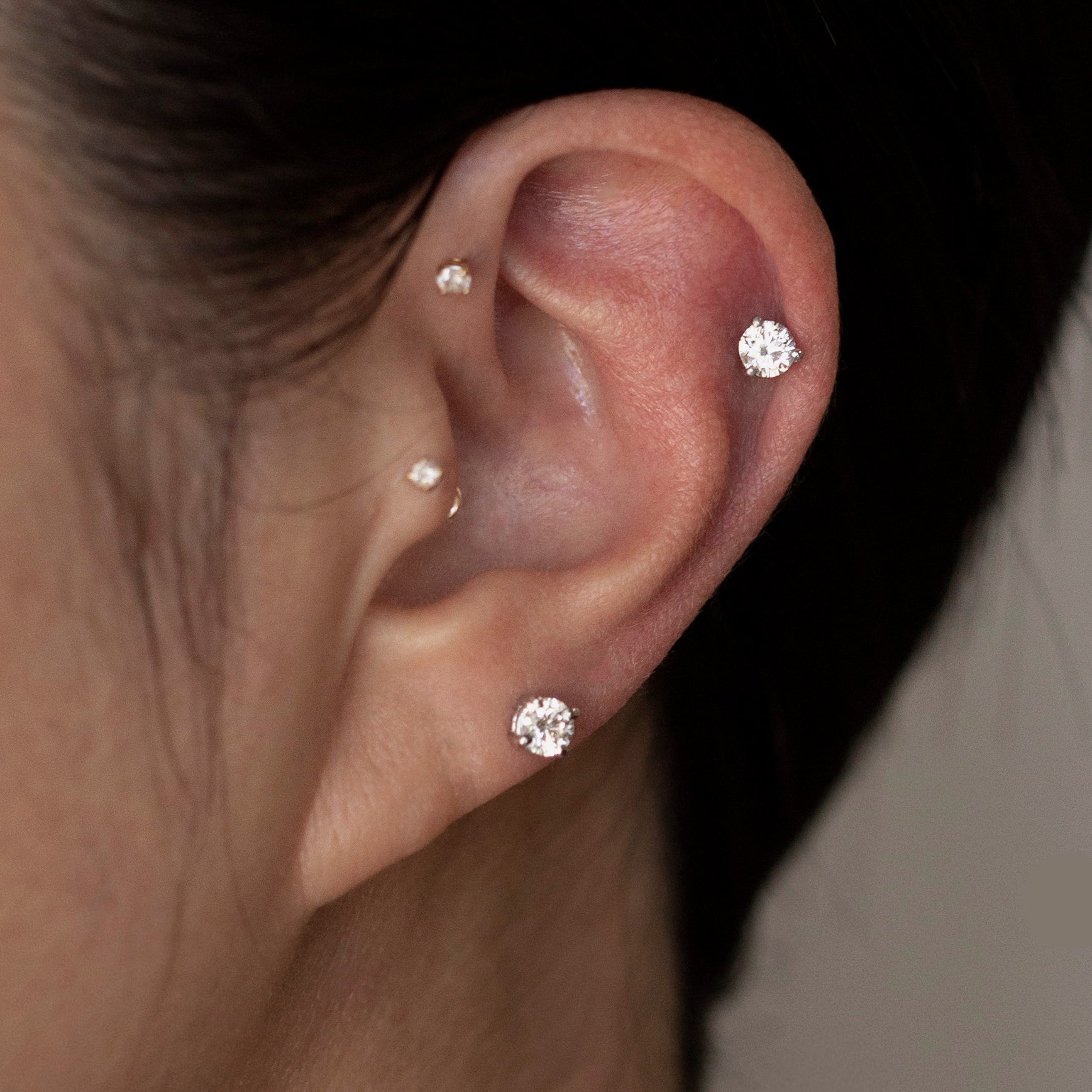 Close-up of an ear wearing three diamond stud earrings with a blurred background.