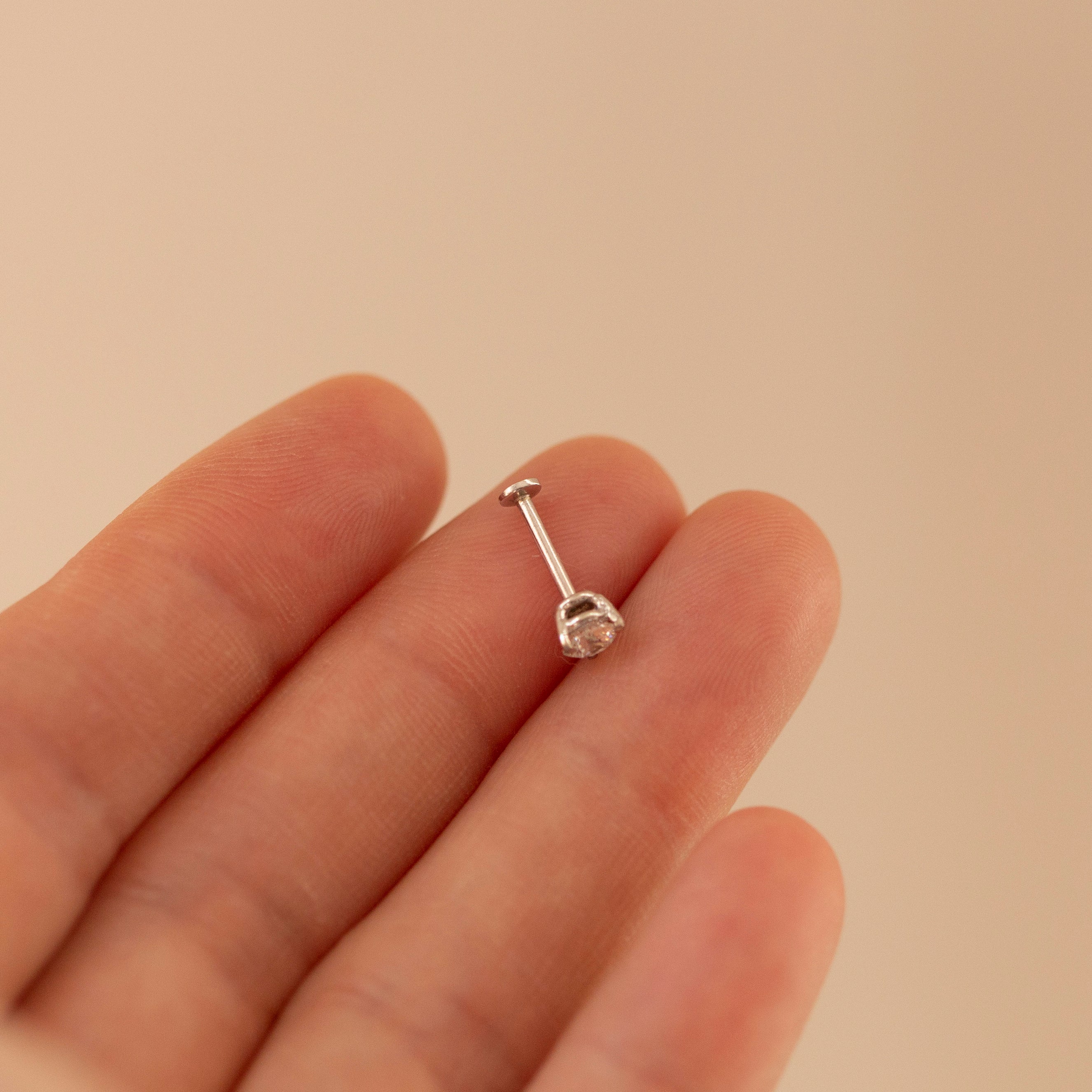 Silver barbell earring on a hand against a beige background
