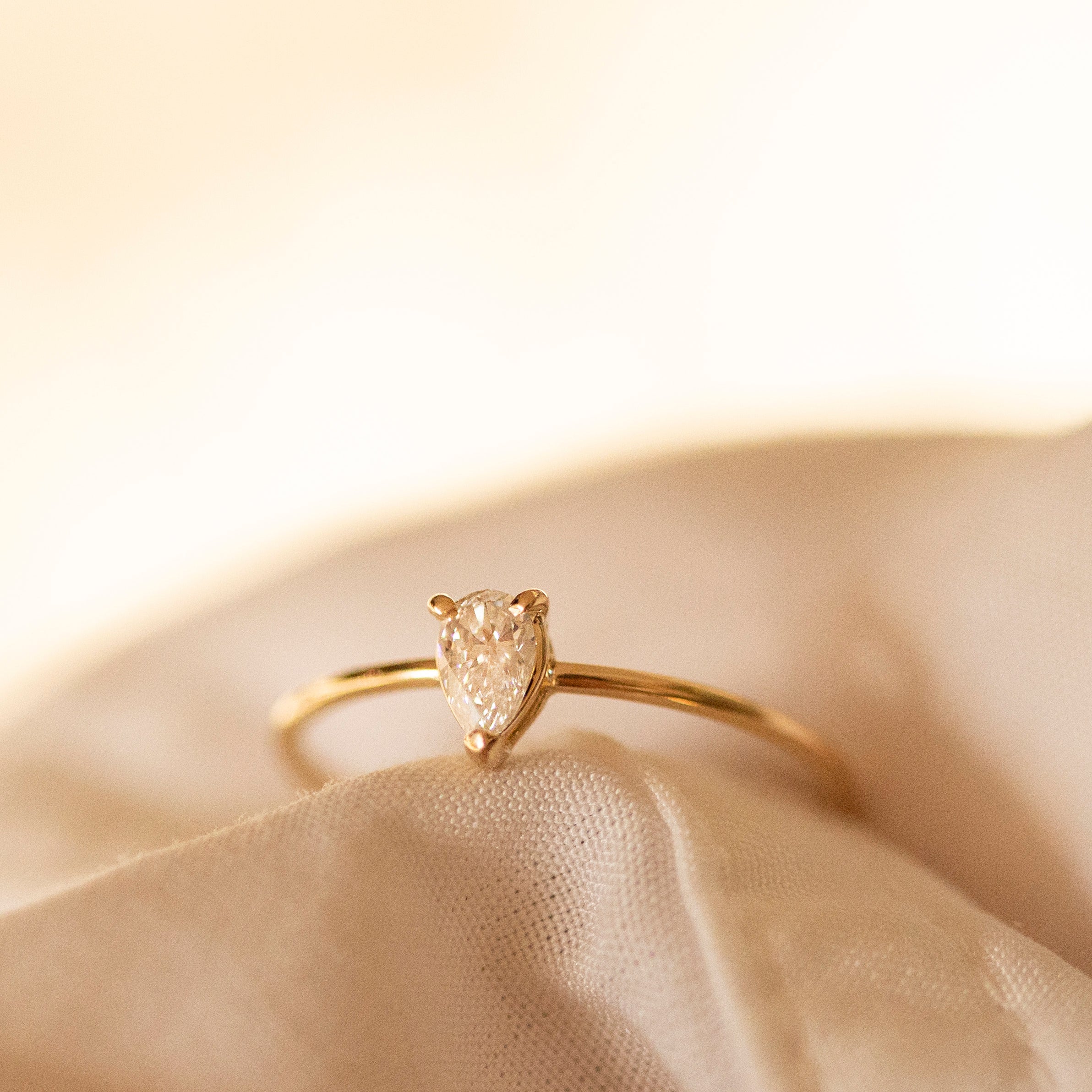 Gold ring with a heart-shaped diamond on a beige fabric background