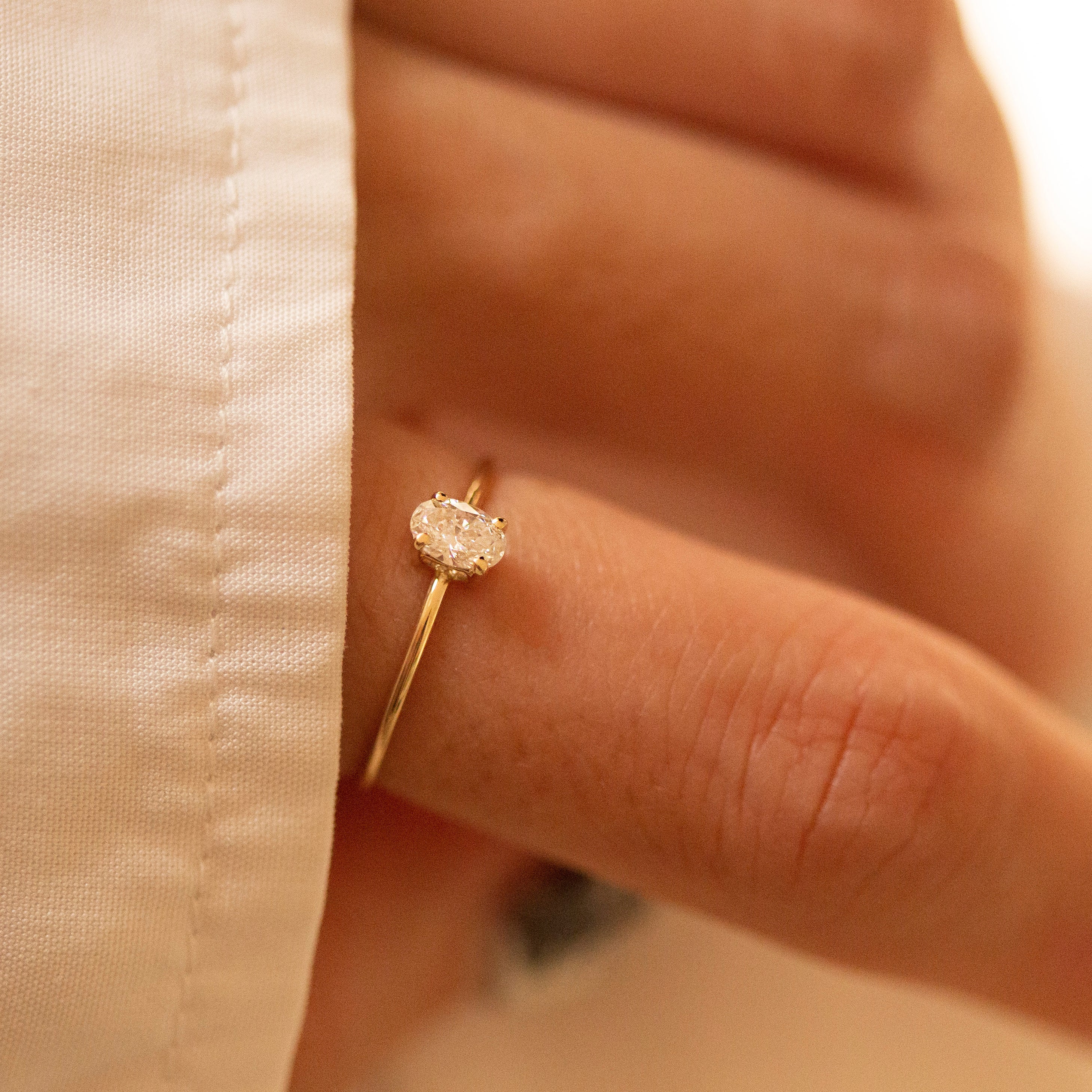 Gold ring with a diamond on a person's finger against a beige fabric background