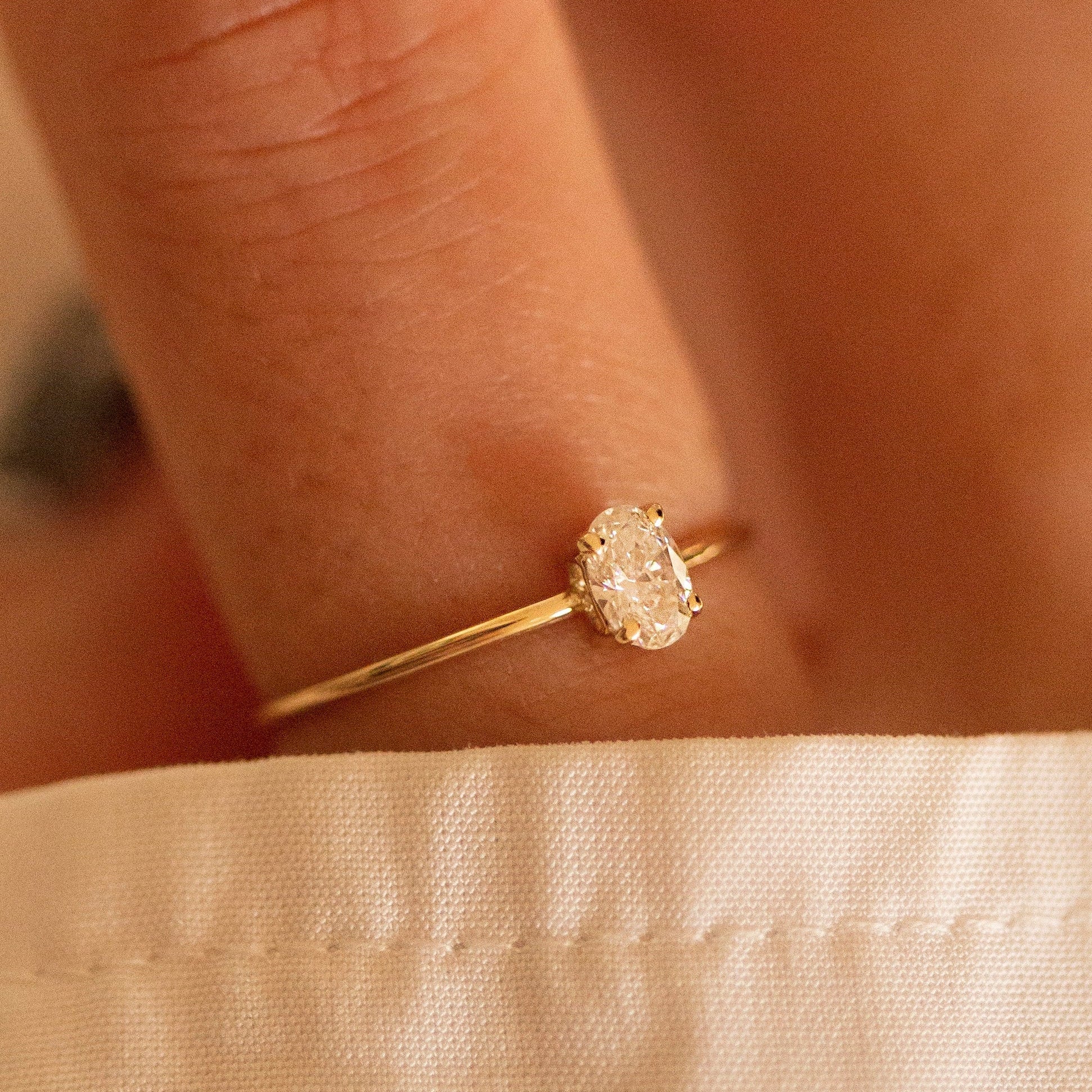 Gold ring with a diamond on a person's finger against a beige fabric background