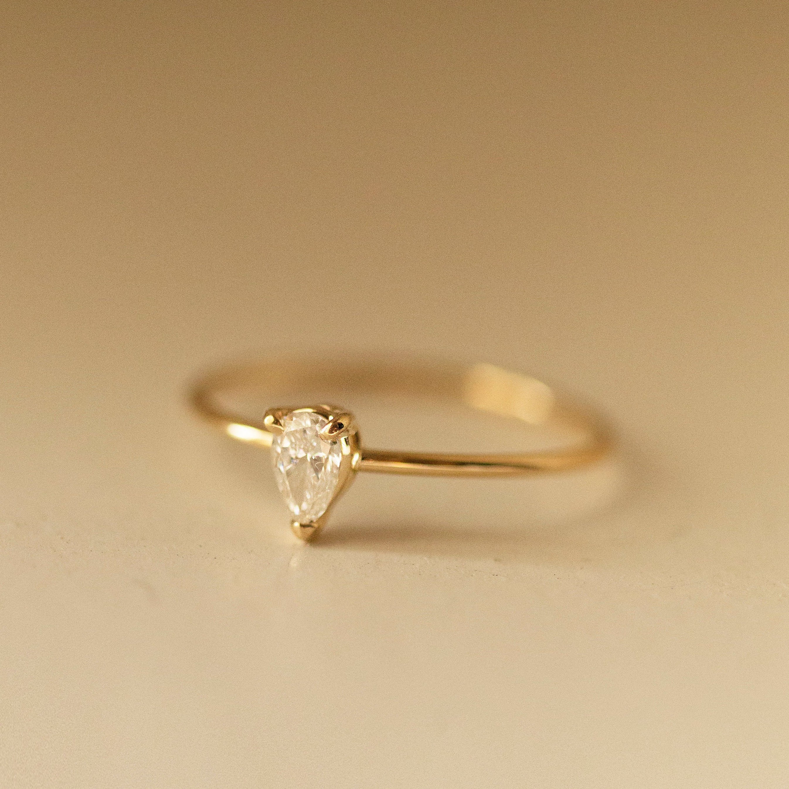 Gold ring with a pear-shaped diamond on a beige background