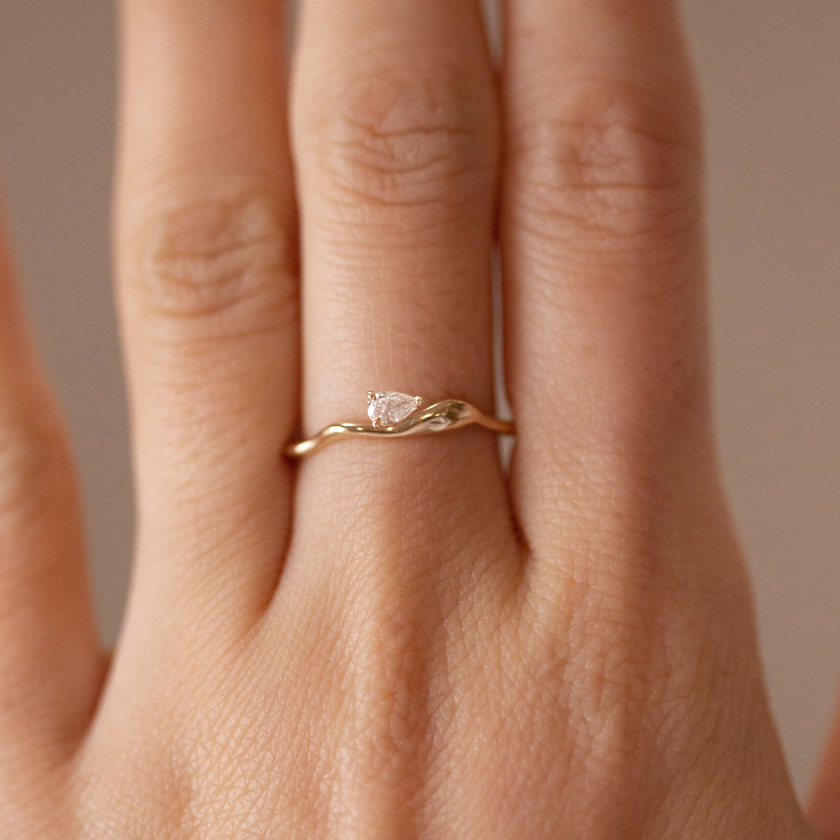 Gold ring with a diamond on a person's finger against a neutral background