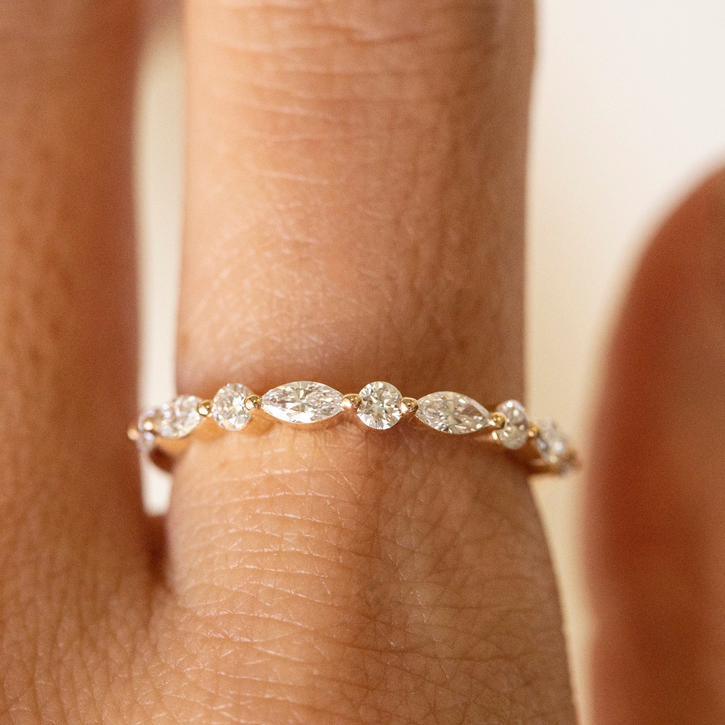 A close-up of a delicate gold ring with a row of small marquise-cut and round clear gemstones worn on a finger.