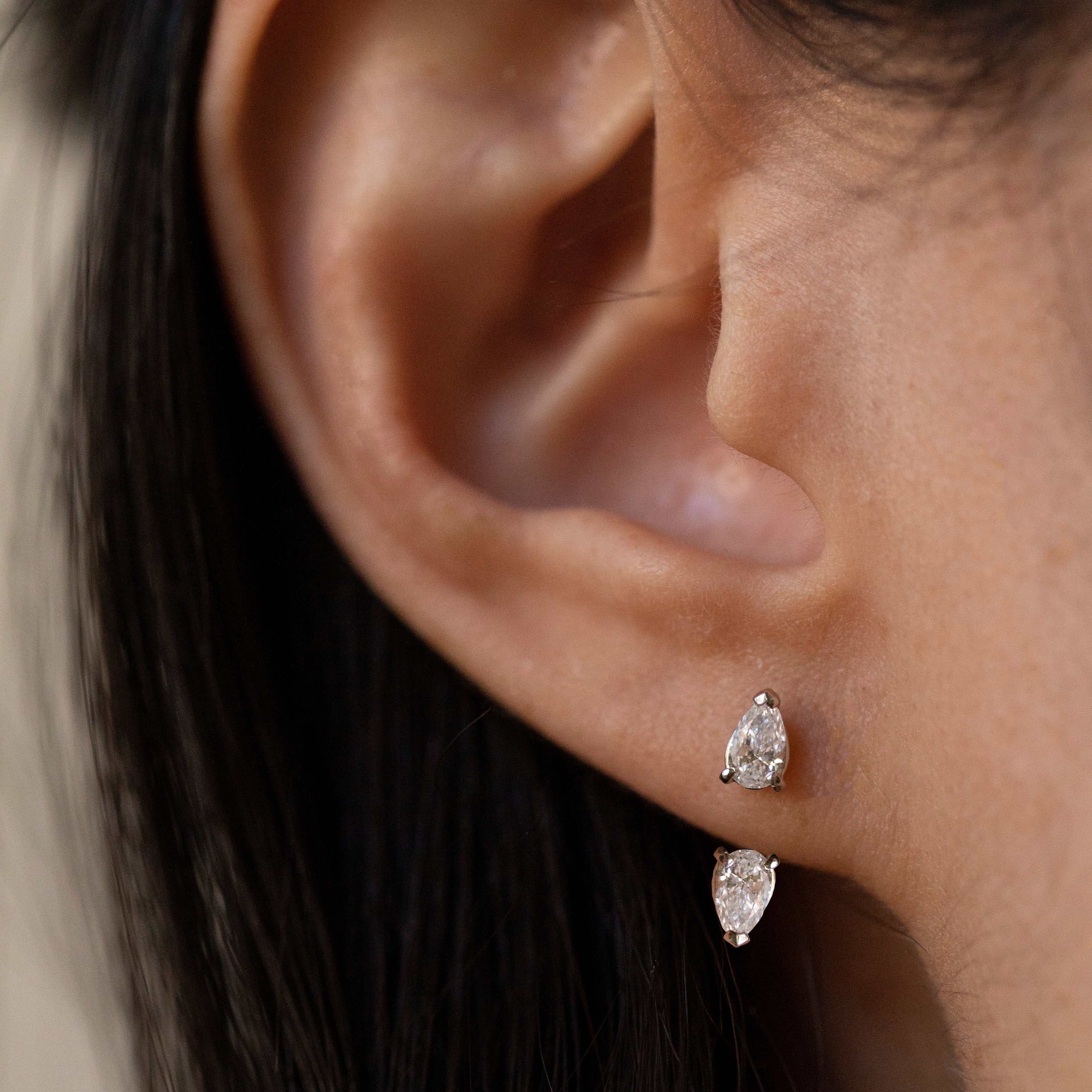 Close-up of a person's ear wearing a pair of silver-tone drop earrings with marquise-cut clear stones.
