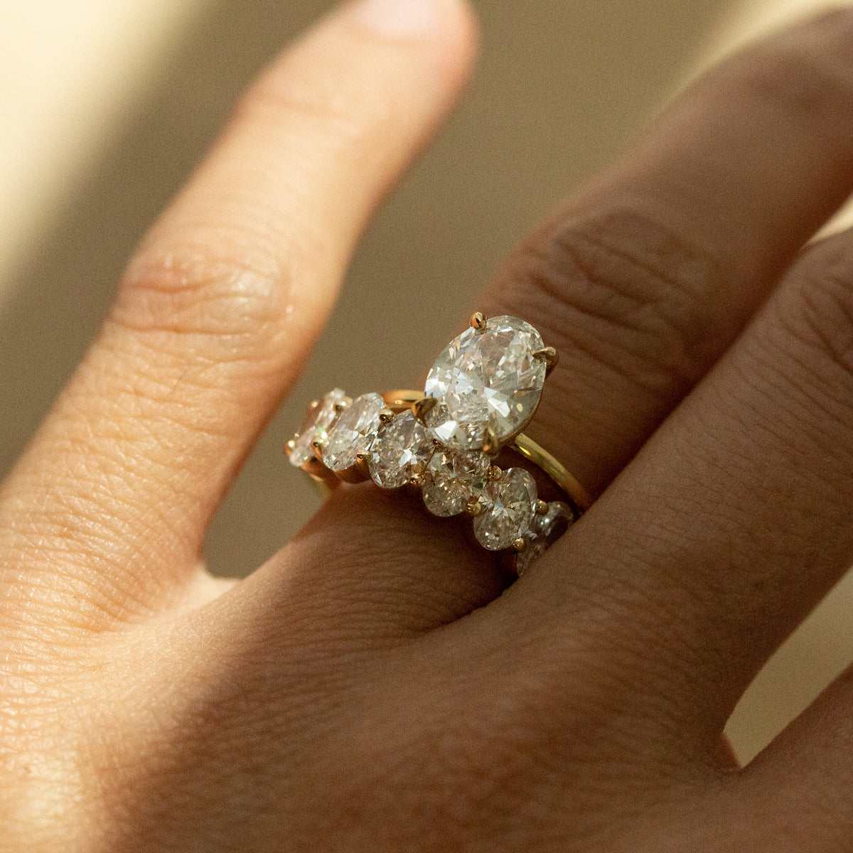 A close-up of a hand wearing a yellow gold ring set with multiple clear diamonds, including a prominent marquise-cut center stone.
