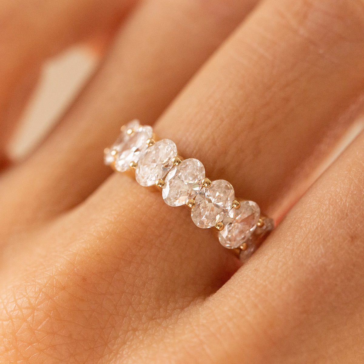 A close-up of a hand wearing a delicate gold band ring set with five round-cut clear stones.