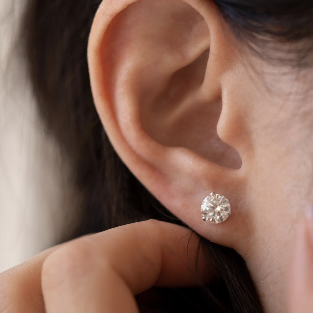 Close-up of an ear wearing a diamond stud earring with a blurred background