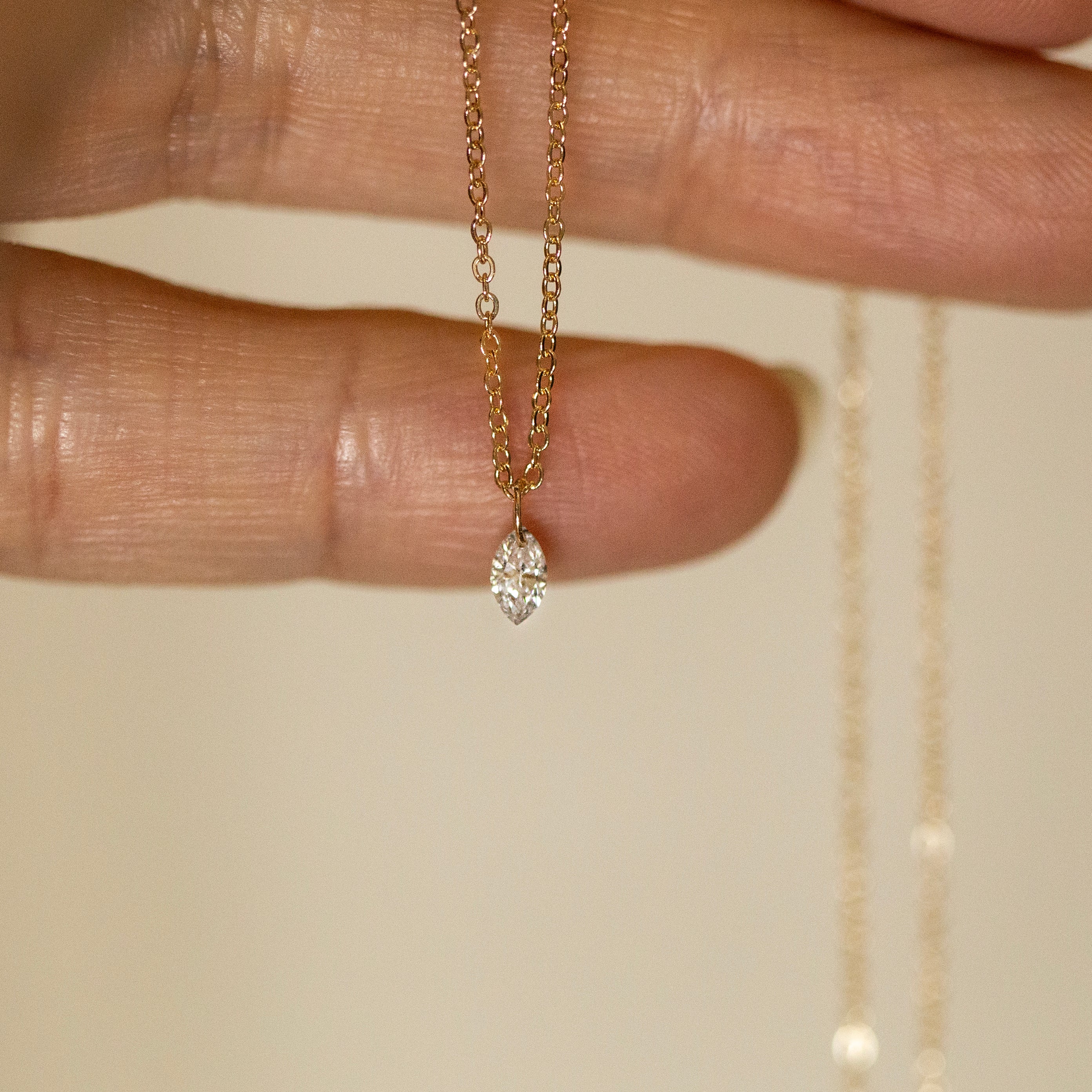 Gold necklace with a diamond pendant held between fingers on a neutral background