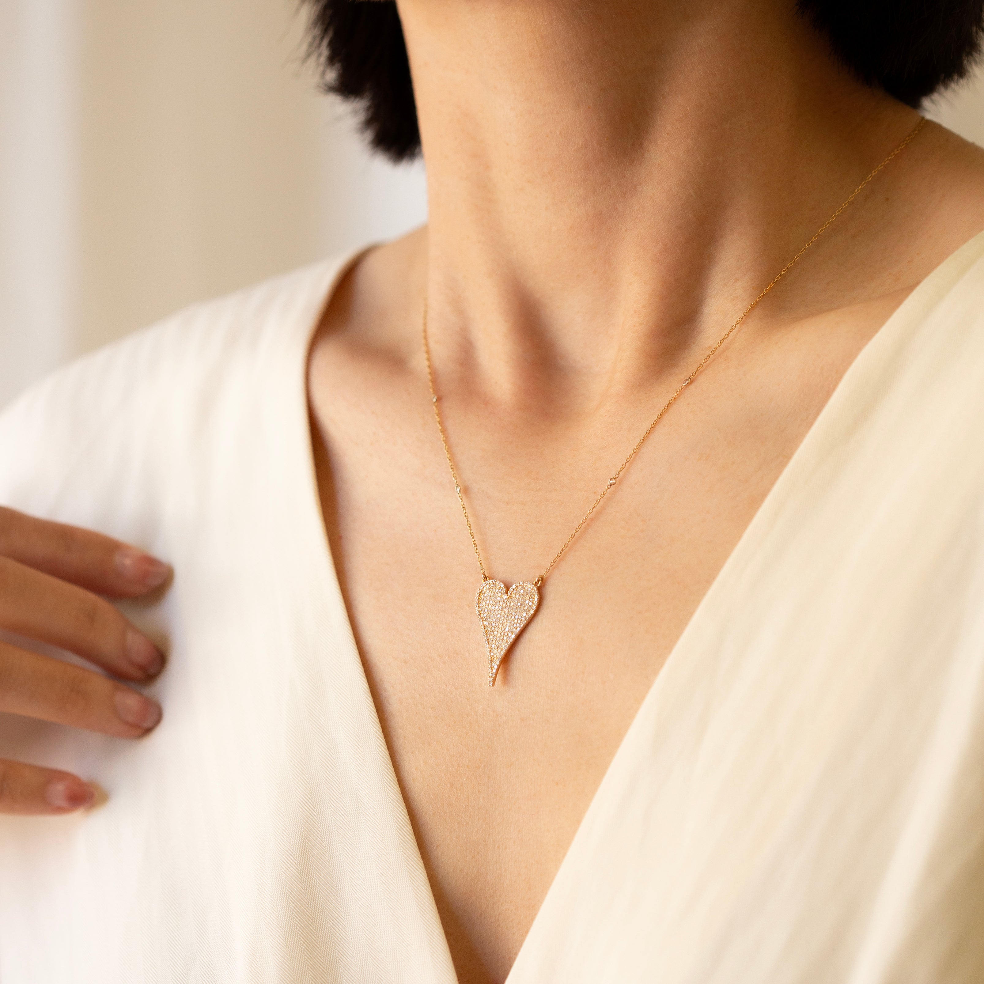 Person wearing a delicate gold necklace with a heart pendant against a neutral background