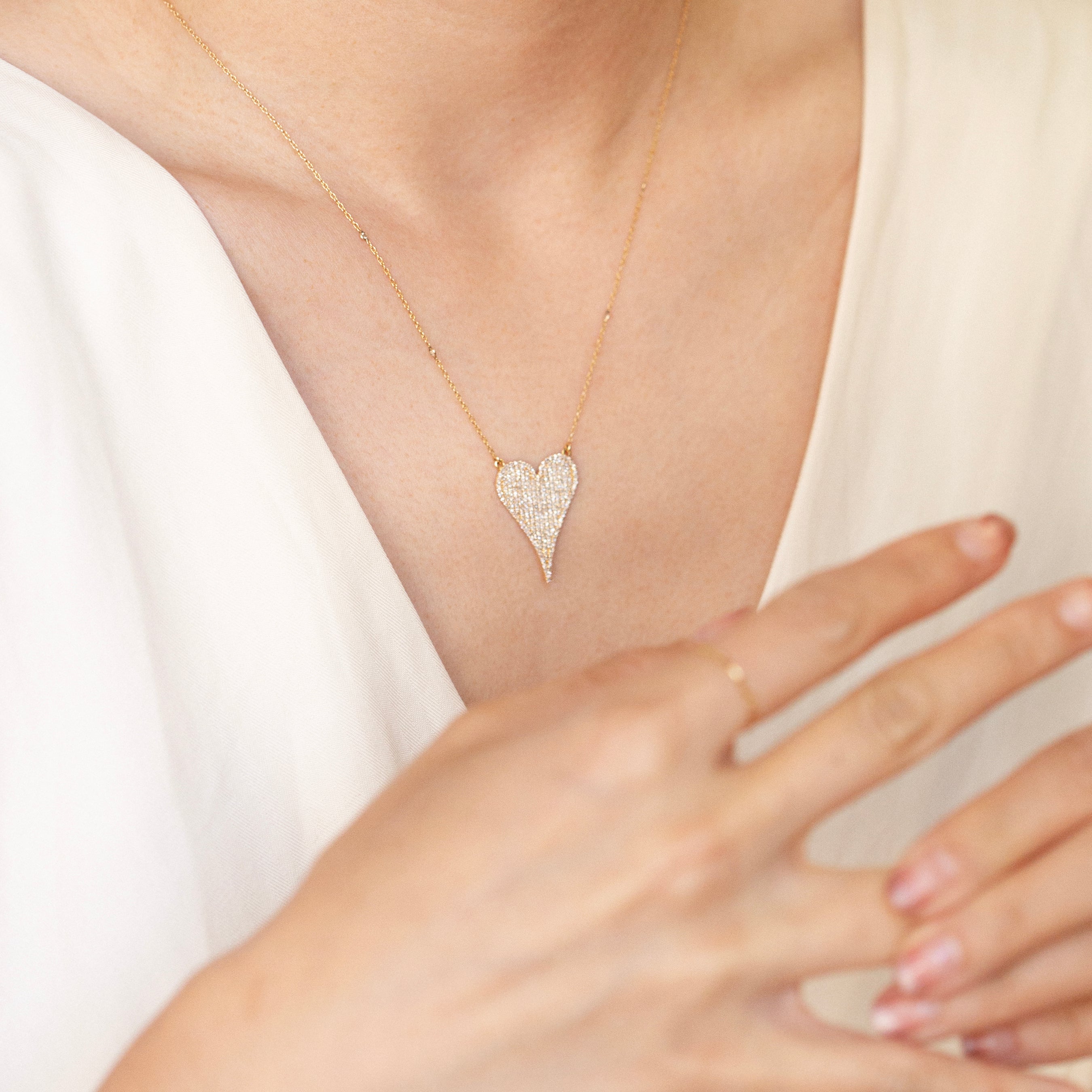 Heart-shaped diamond necklace worn by a person in a white dress.