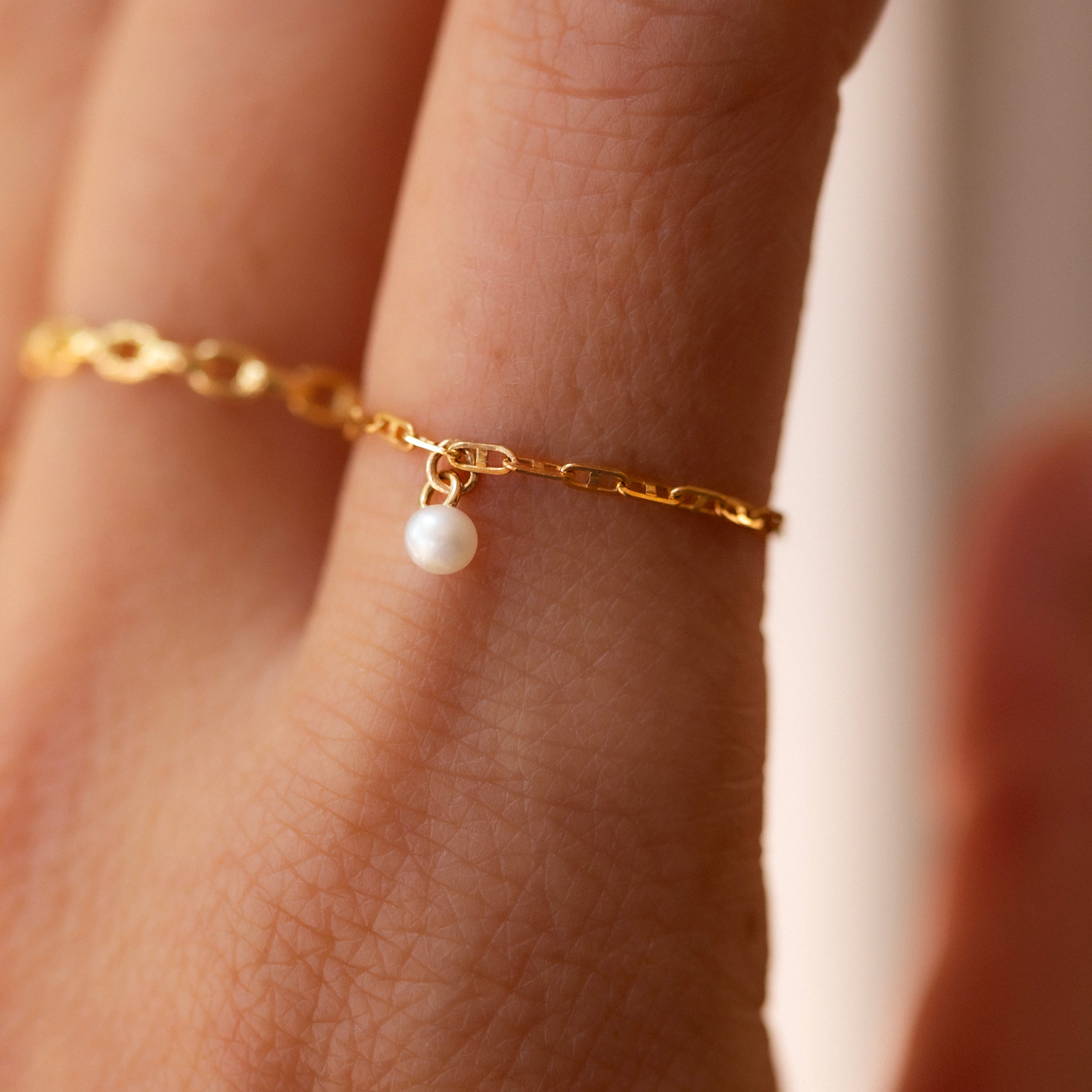 This 14k Solid Gold Chain Ring features a delicate link design and a dainty dangling pearl, creating a modern yet timeless accessory. Worn solo or paired with other rings, it adds a touch of elegance to any look. 