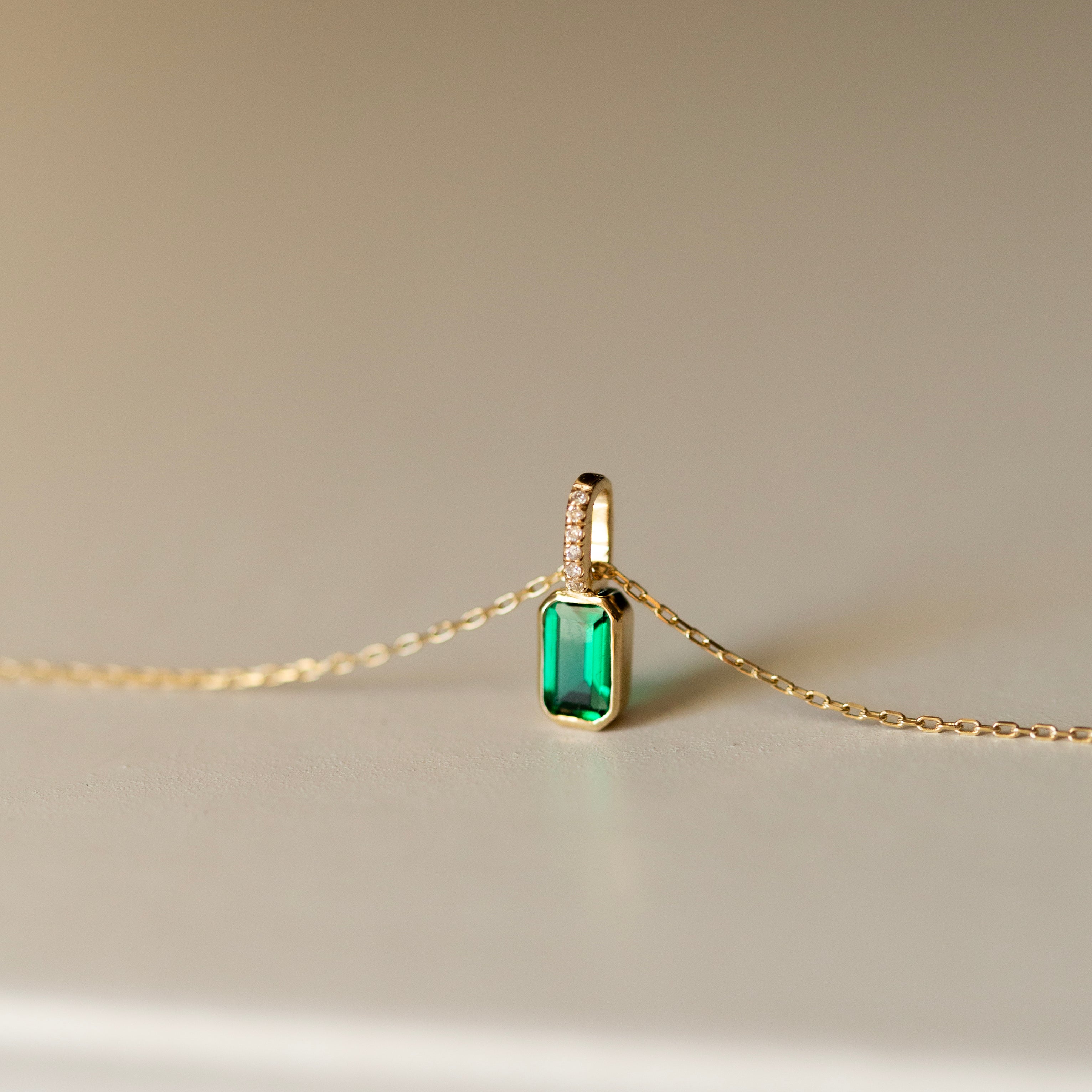 Gold necklace with a green gemstone pendant on a beige background