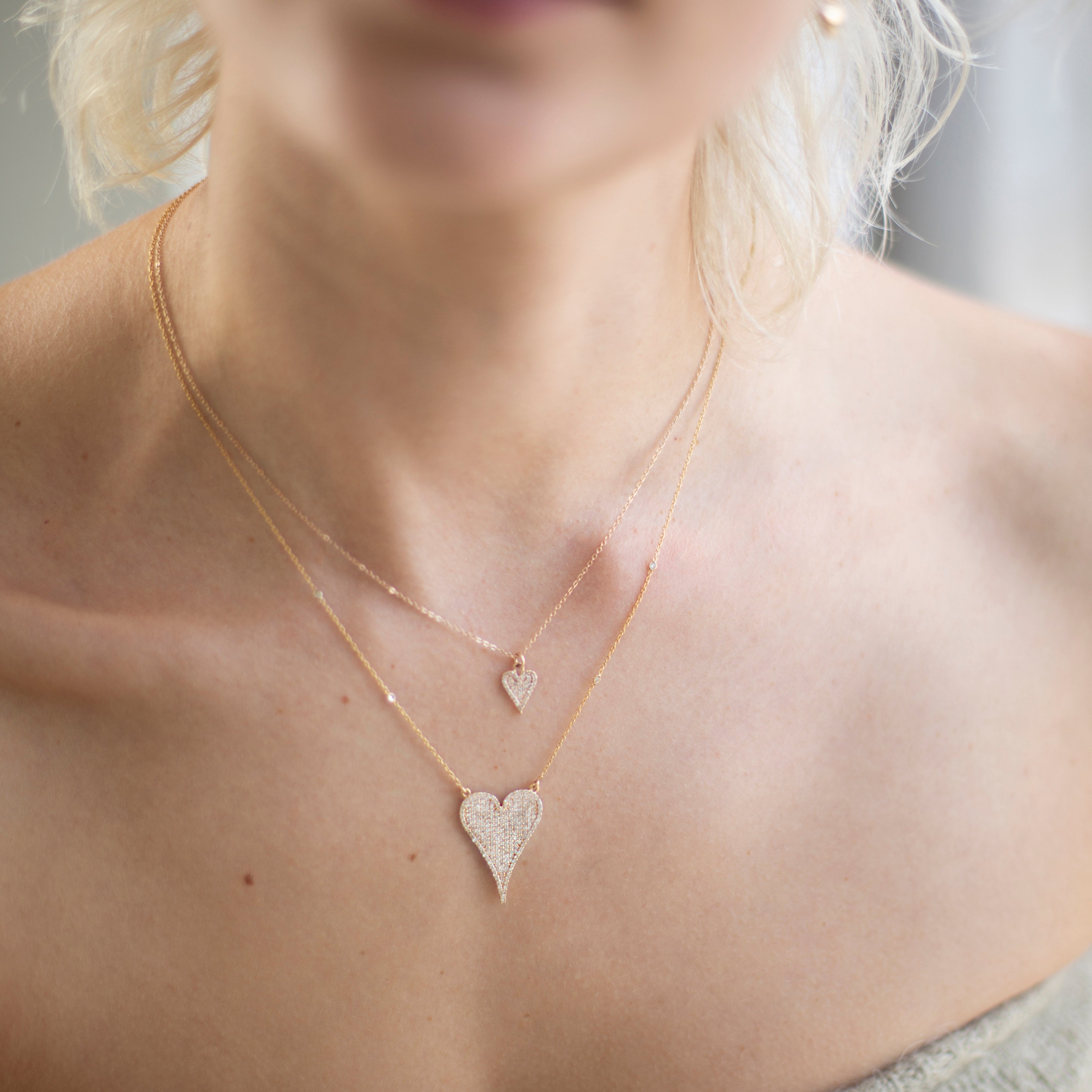 Close-up of a person wearing two heart-shaped necklaces.