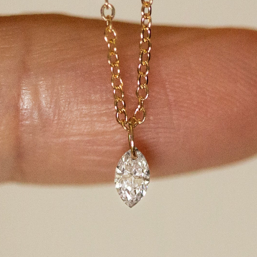 Gold necklace with a diamond pendant held between fingers on a neutral background