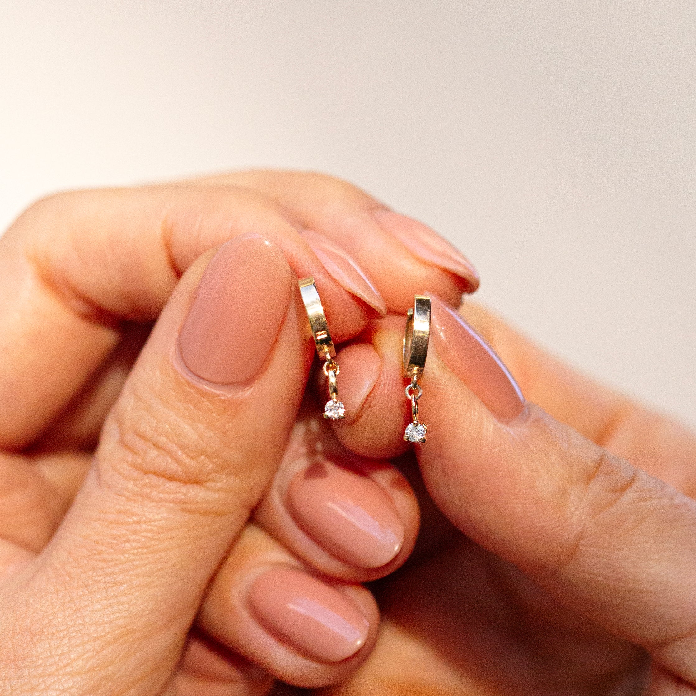 Diamond dangle hoop earrings held by hand.