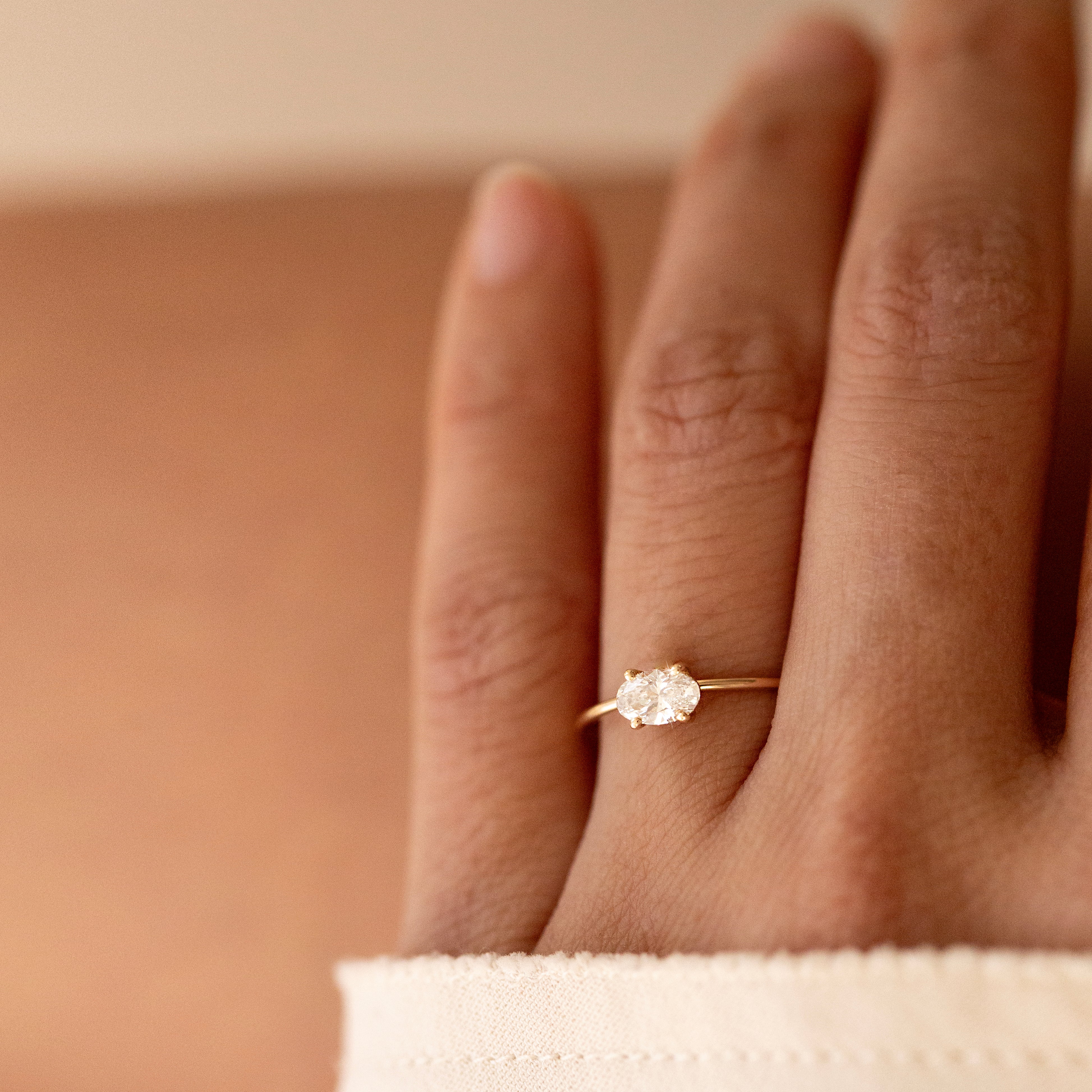 Hand wearing a diamond ring on a neutral background