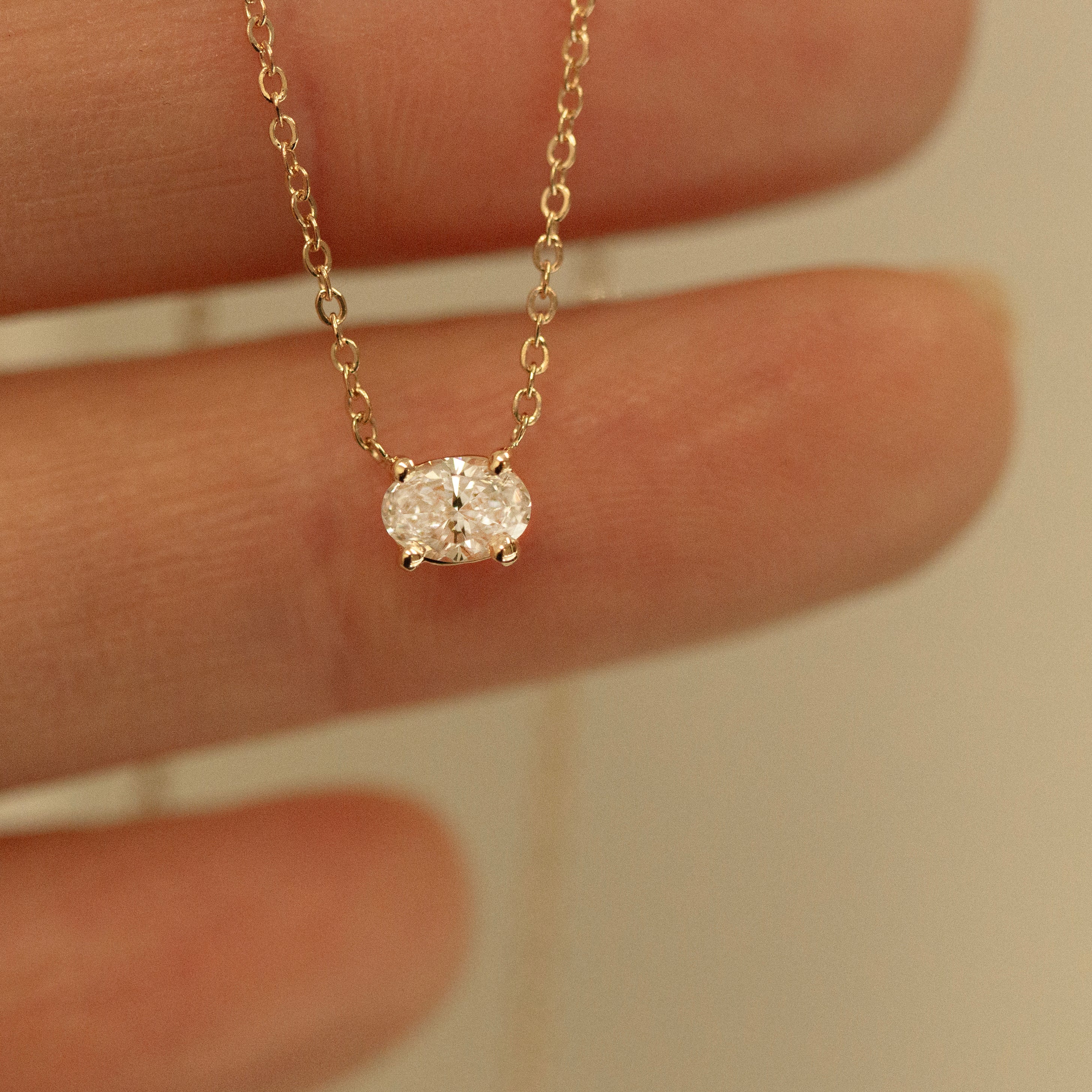 Gold necklace with a small diamond pendant held between fingers against a neutral background