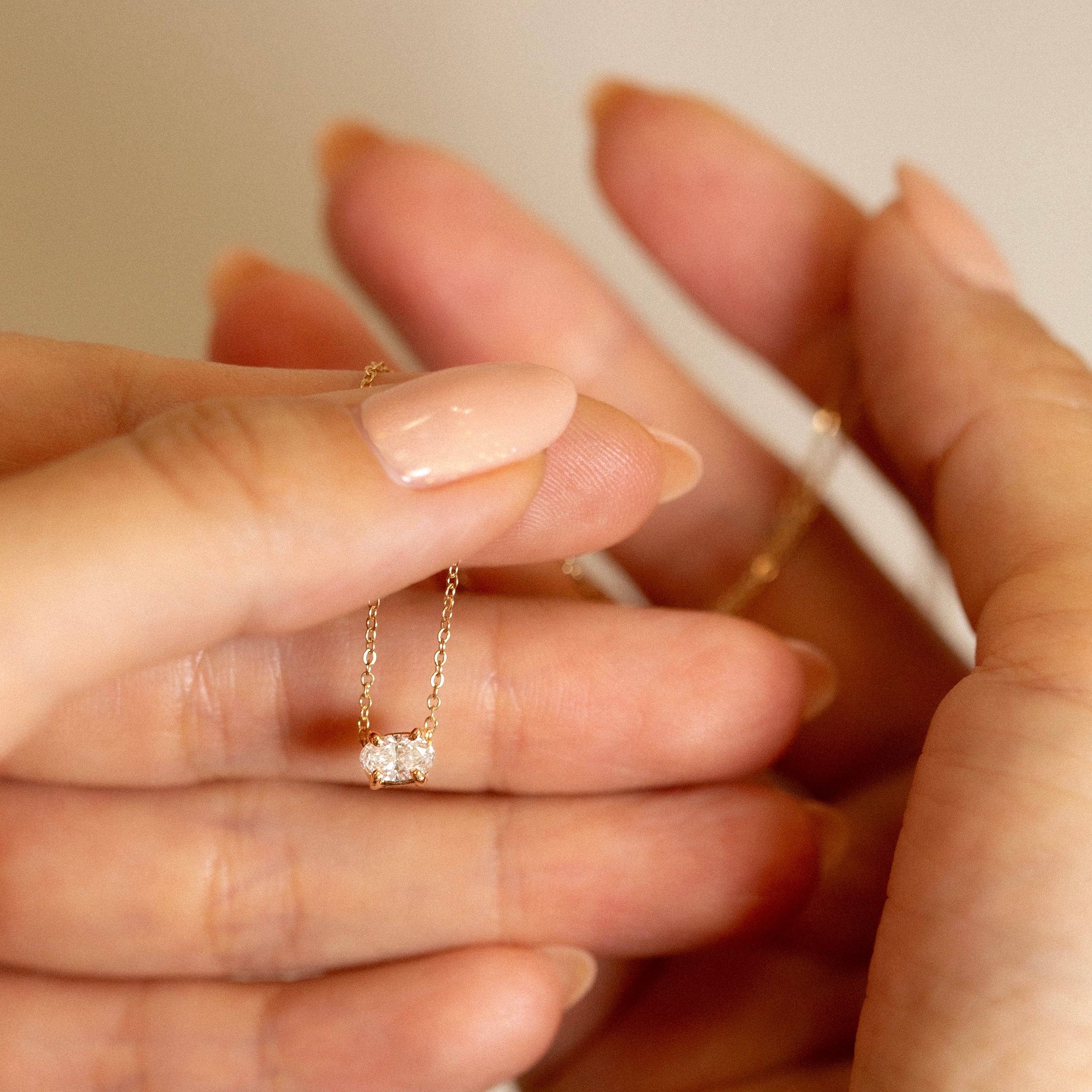 Close-up of a hand wearing a delicate gold ring with a small diamond on a neutral background