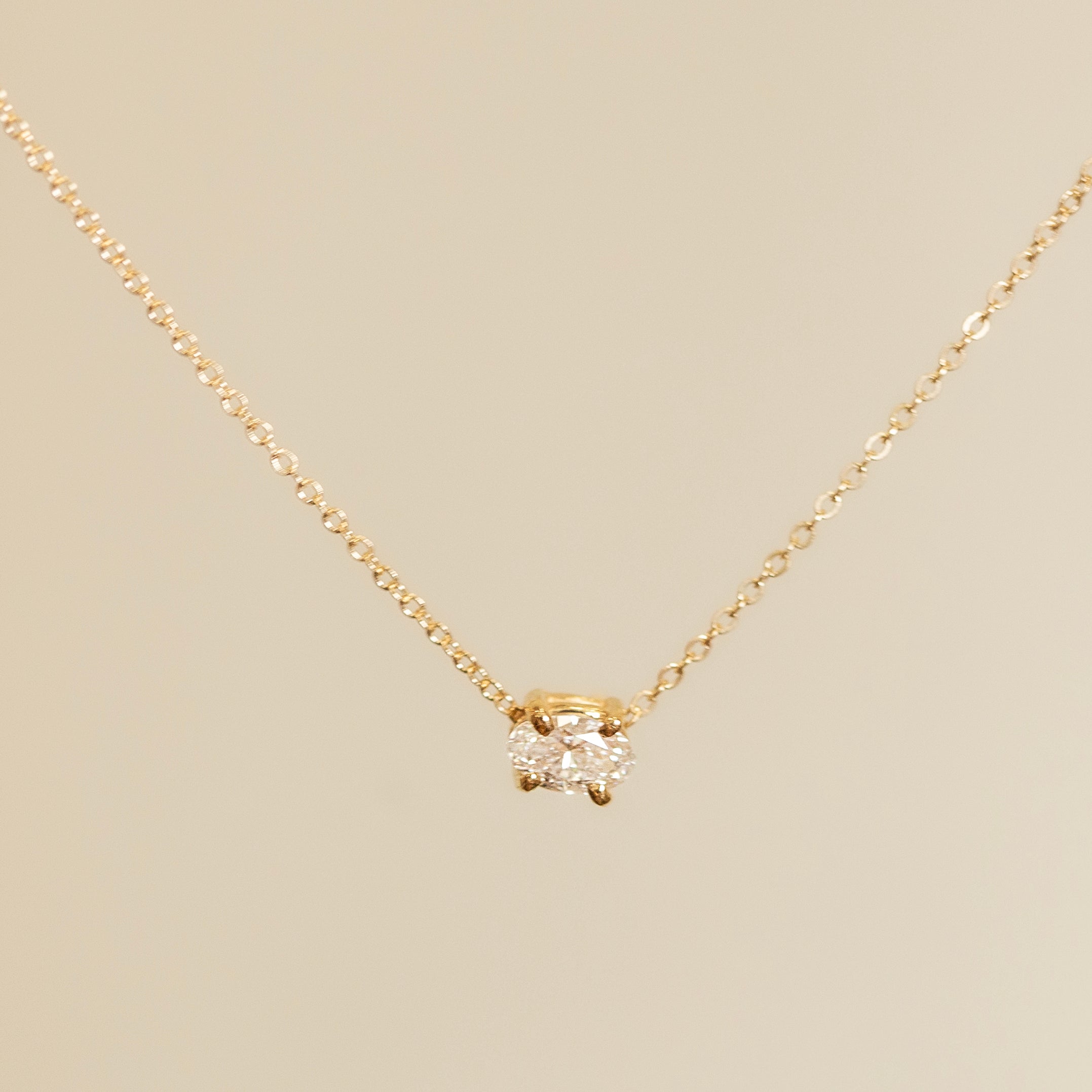Gold necklace with a diamond pendant on a beige background