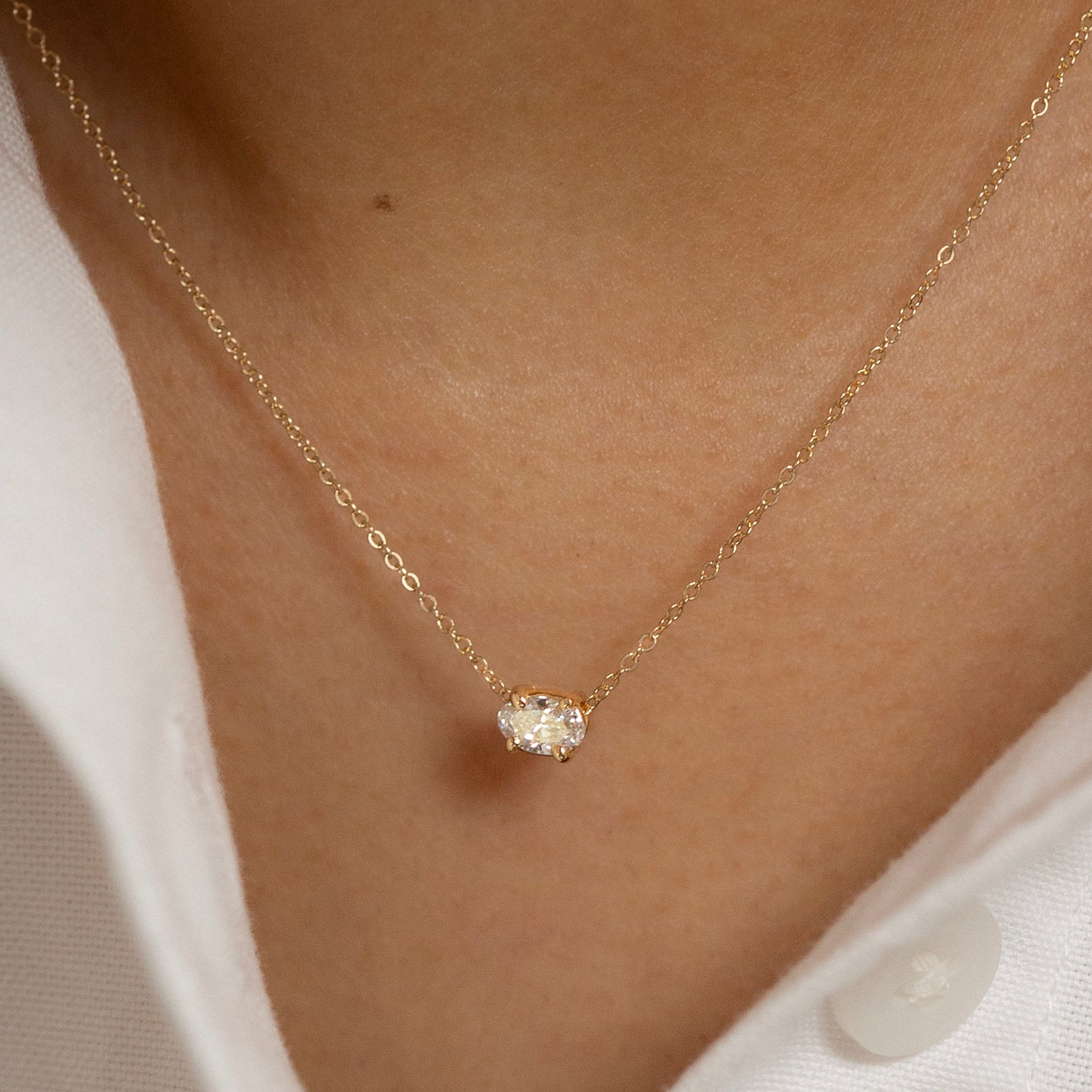 Gold necklace with a small diamond pendant on a person wearing a white shirt.