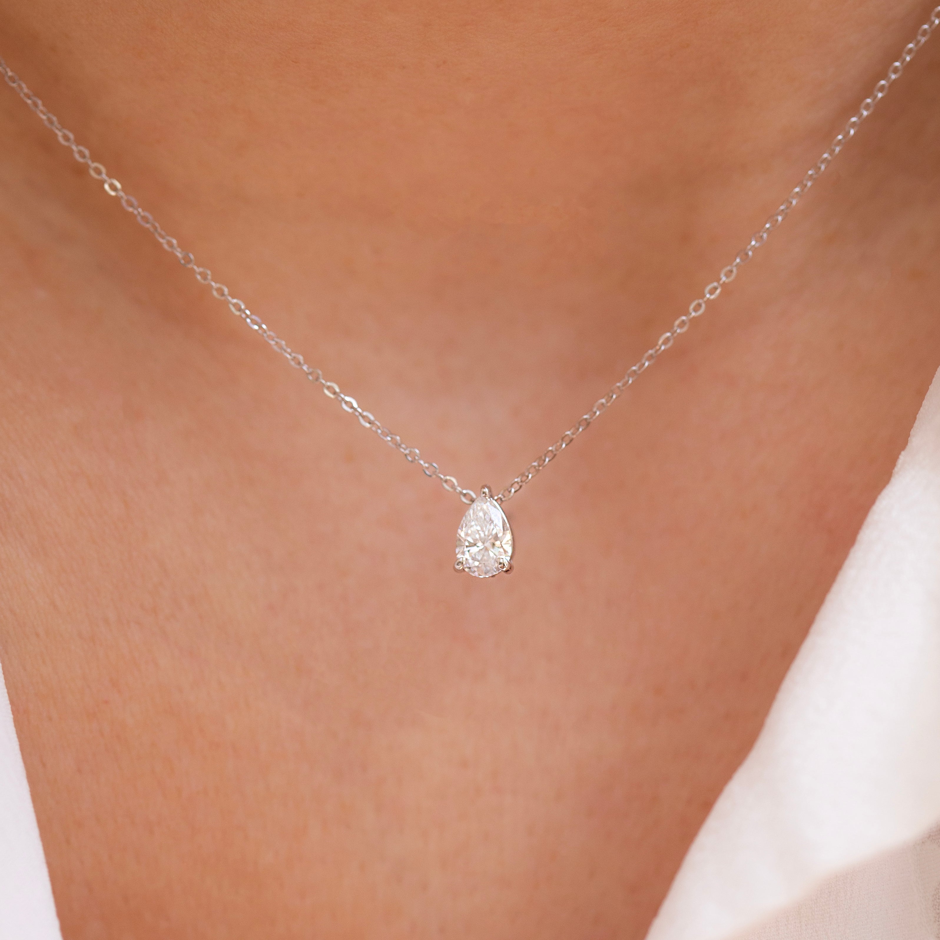 A close-up image of a woman's neck wearing a pear cut diamond solitaire necklace set in a 3-prong setting on a gold chain.