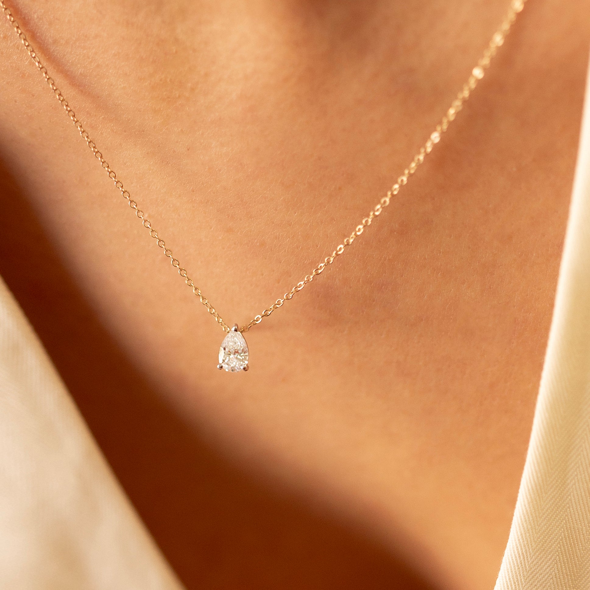 Gold necklace with a teardrop-shaped diamond pendant on a soft beige background