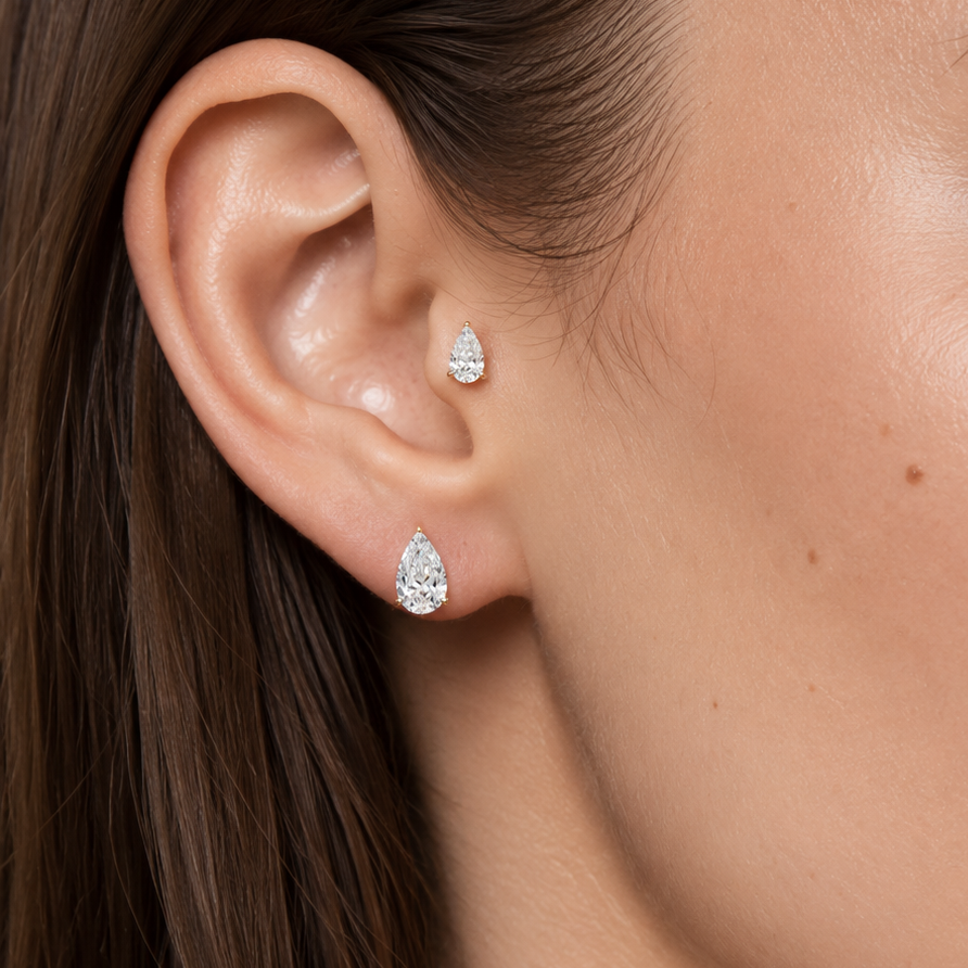 Close-up of a woman's ear wearing two small pear-shaped stud earrings with clear sparkling stones.