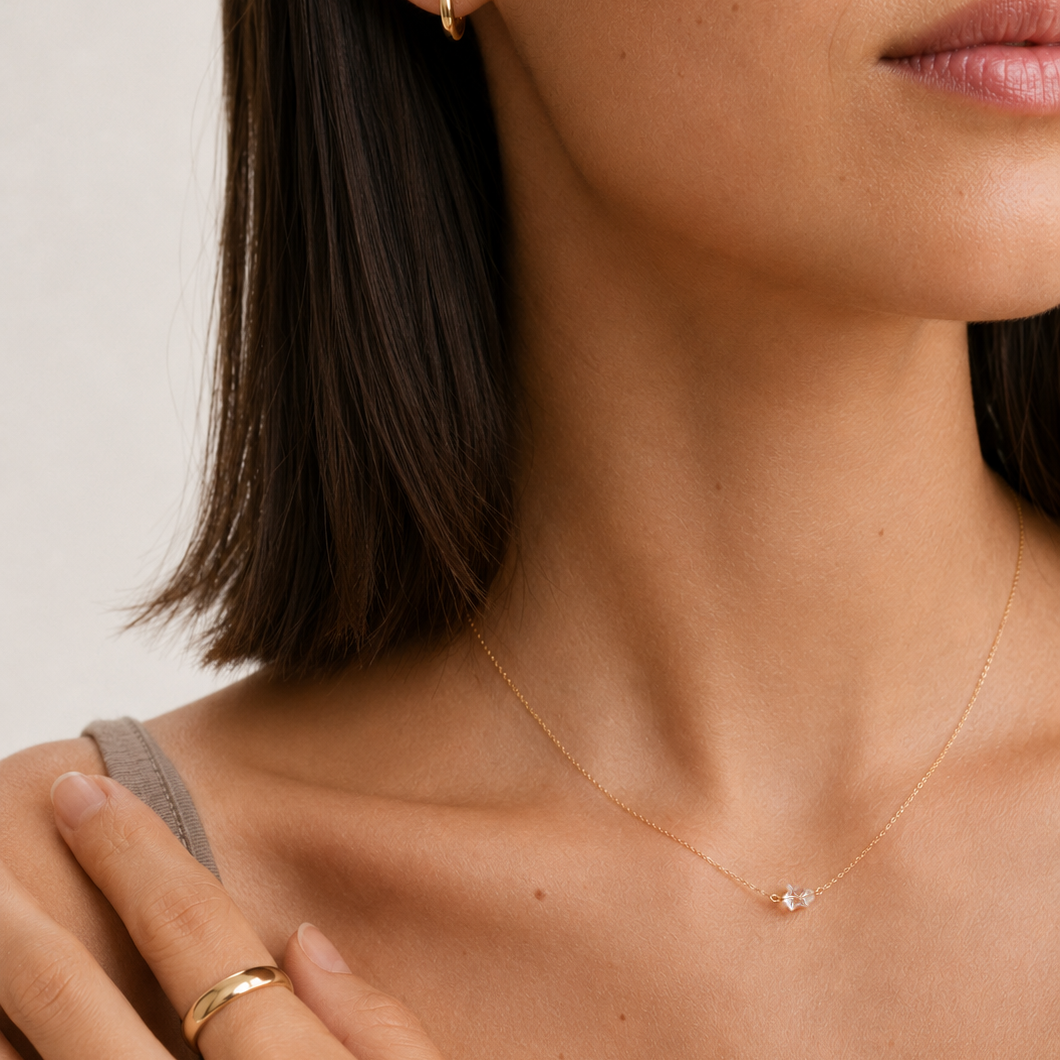 Close-up of a woman wearing a delicate gold chain necklace with a small clear stone pendant, along with matching gold rings and a small gold hoop earring.