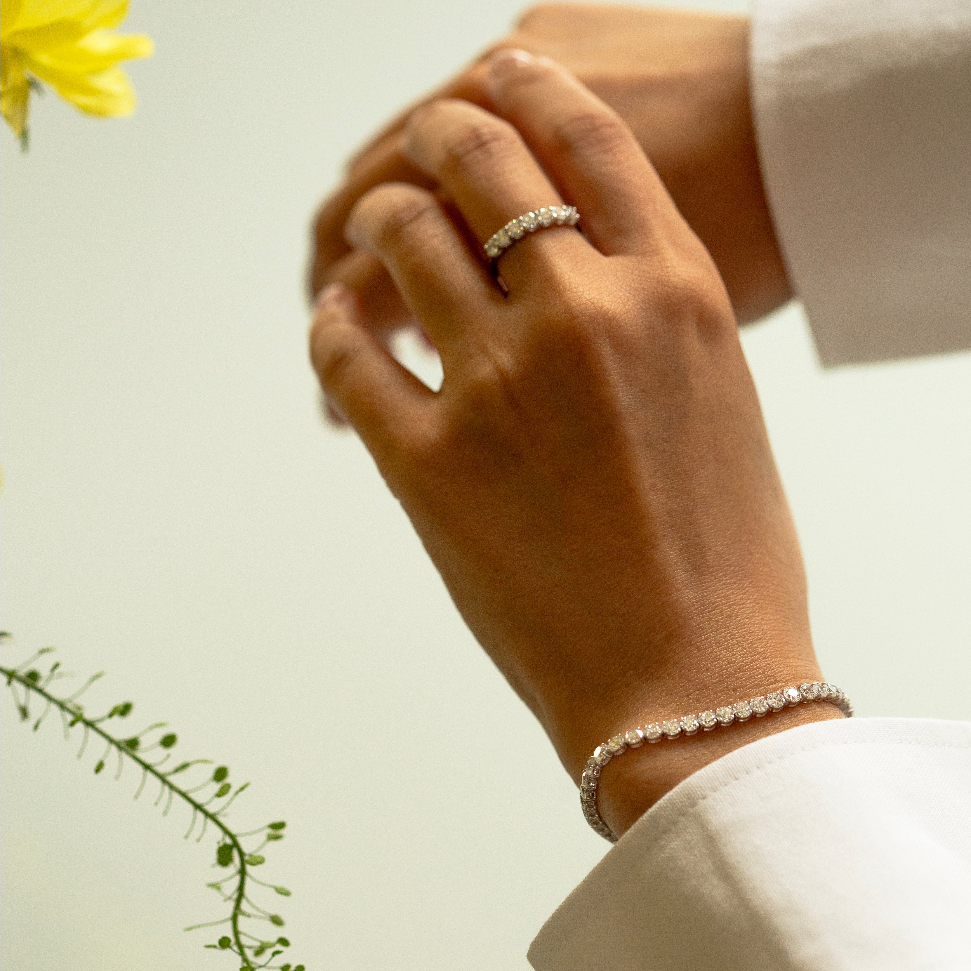 Hand wearing a diamond ring and bracelet with a yellow flower in the background