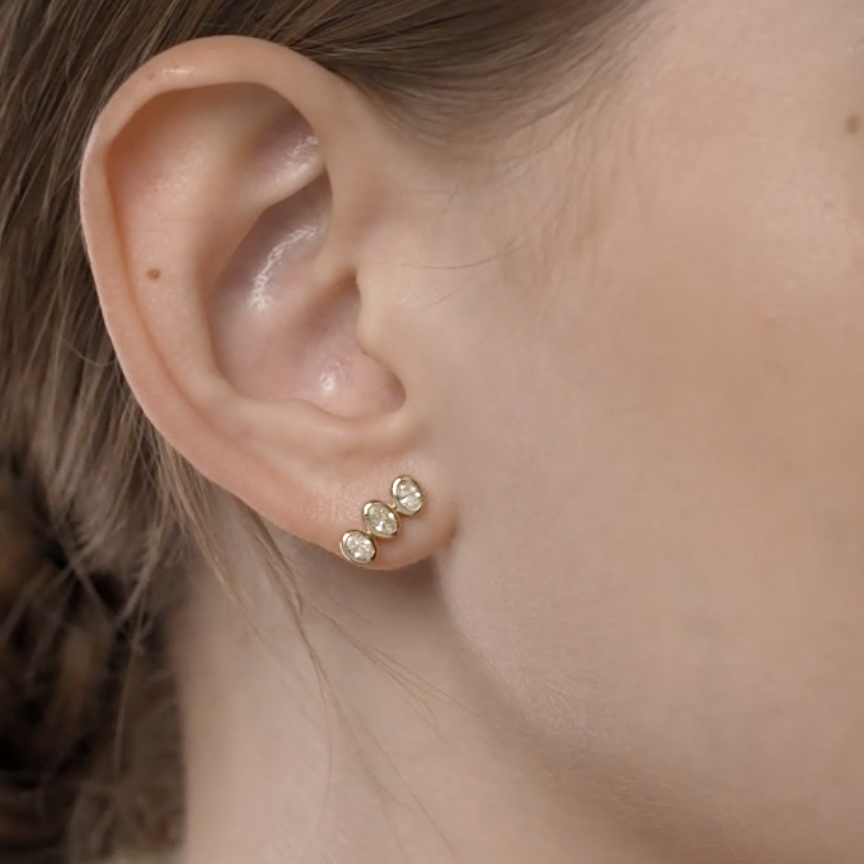 Close-up of an ear wearing gold stud earrings with a blurred background