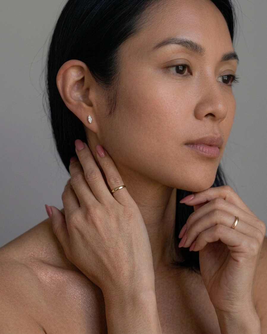 Woman wearing earrings and a ring, with a neutral background
