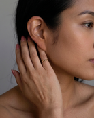 Close-up of a woman's ear with a hand gently touching it, wearing a gold ring.