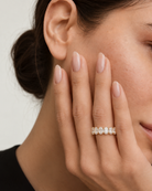 A close-up lifestyle shot of a woman's hand resting against her cheek, wearing a delicate gold ring adorned with small, clear teardrop-cut gemstones.