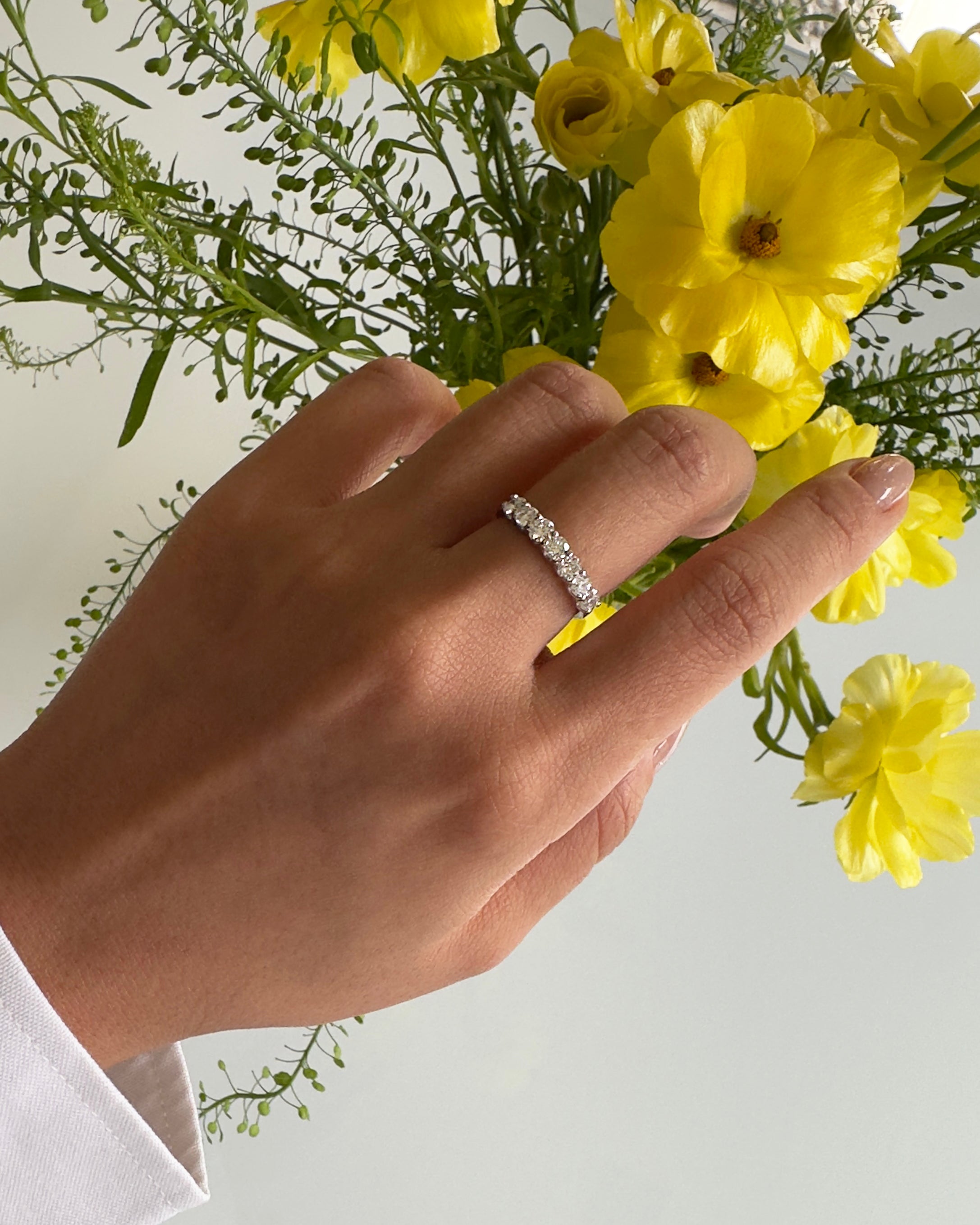 Hand wearing a diamond ring with yellow flowers in the background