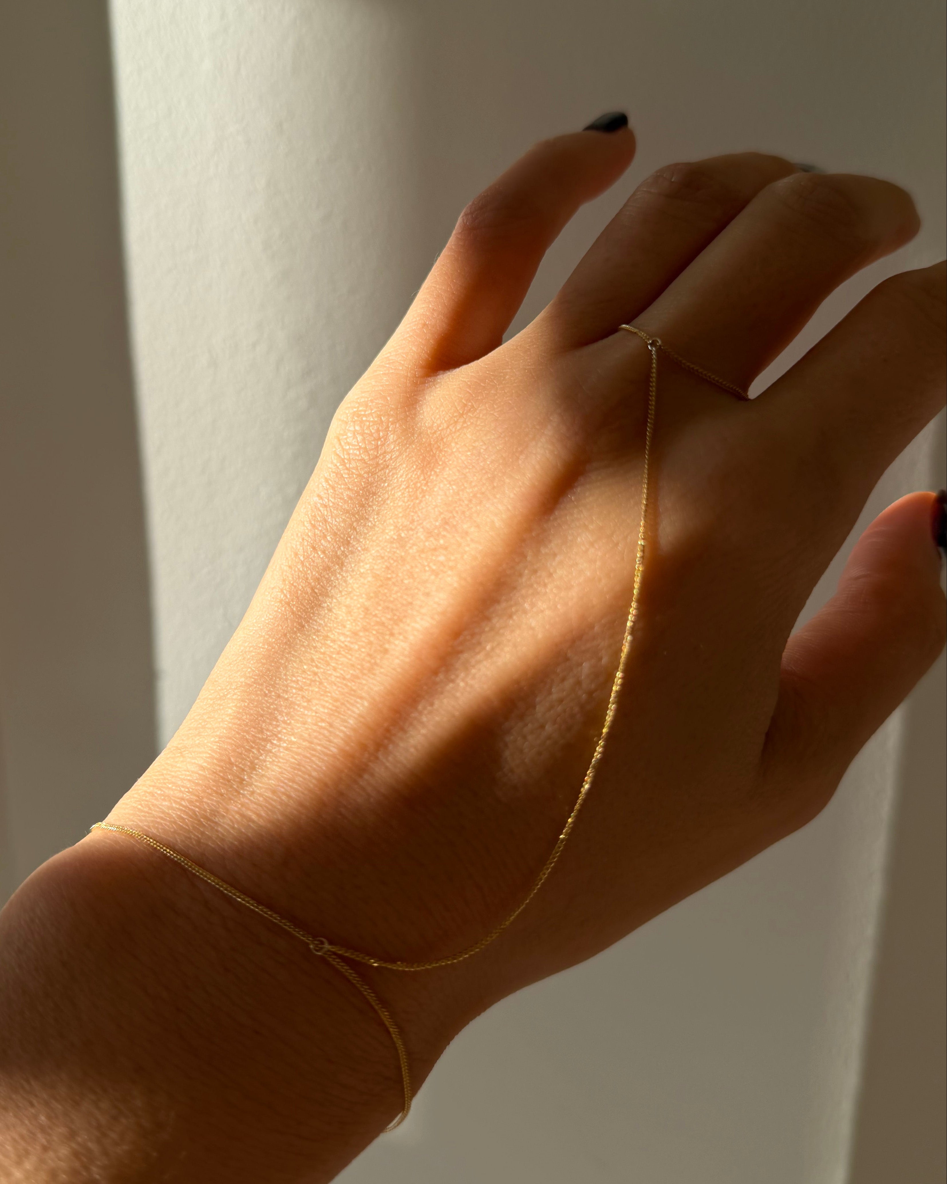 Hand wearing a delicate gold bracelet against a neutral background