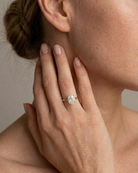Close-up of a hand wearing a diamond ring with a neutral background