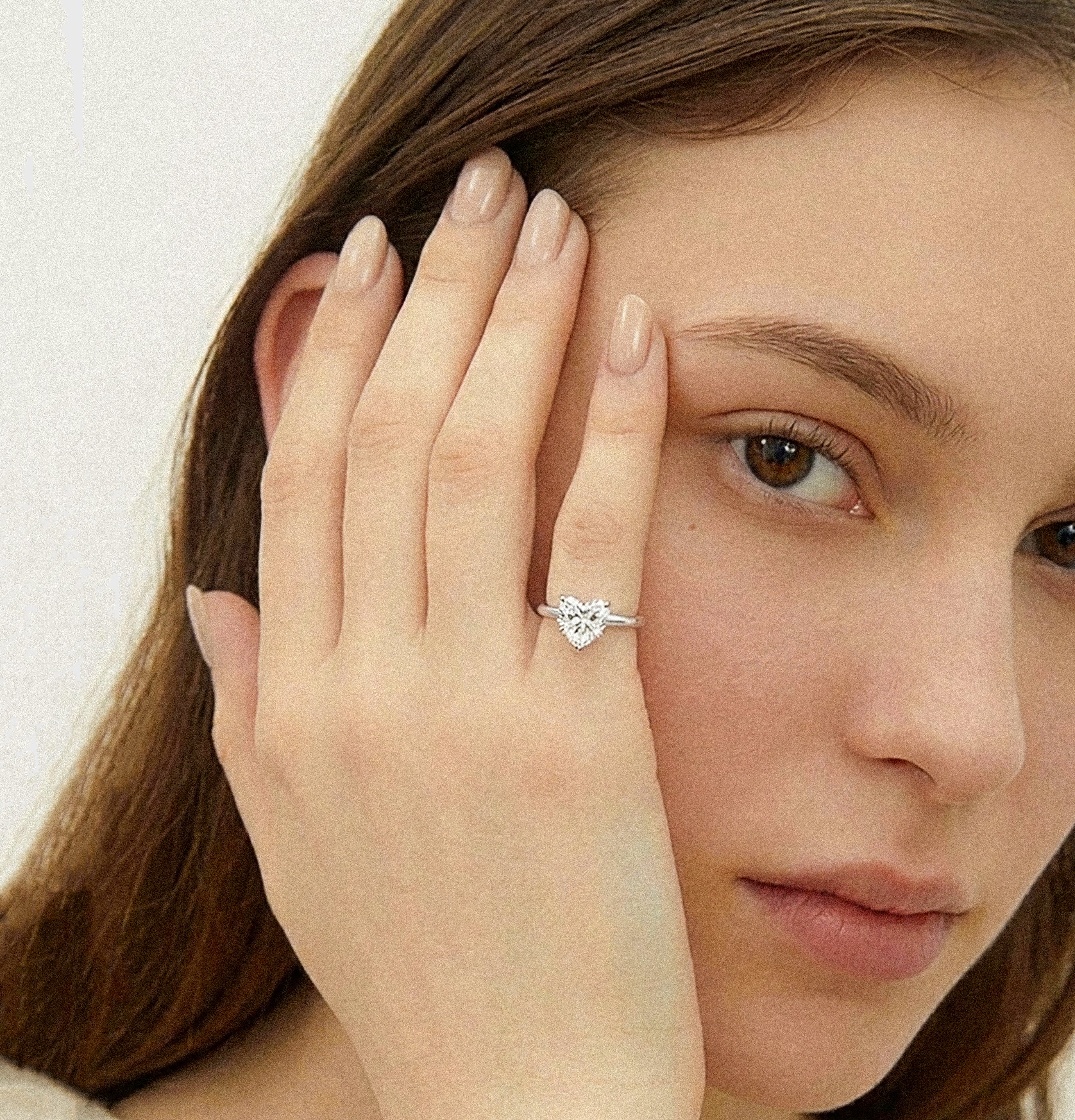 Woman wearing a white gold ring with a heart-shaped diamond on a neutral background
