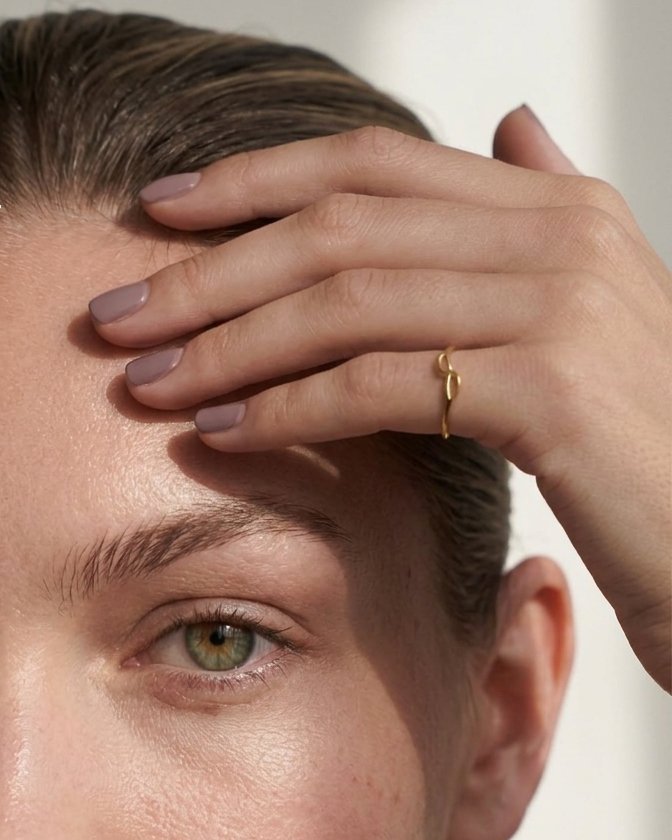 Close-up of a person with a hand on their forehead, wearing a gold ring.